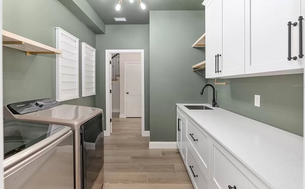 White kitchen cabinets with black handles, black sink and faucet set in a white countertop, wood flooring with white trim, partial view of dryer top.