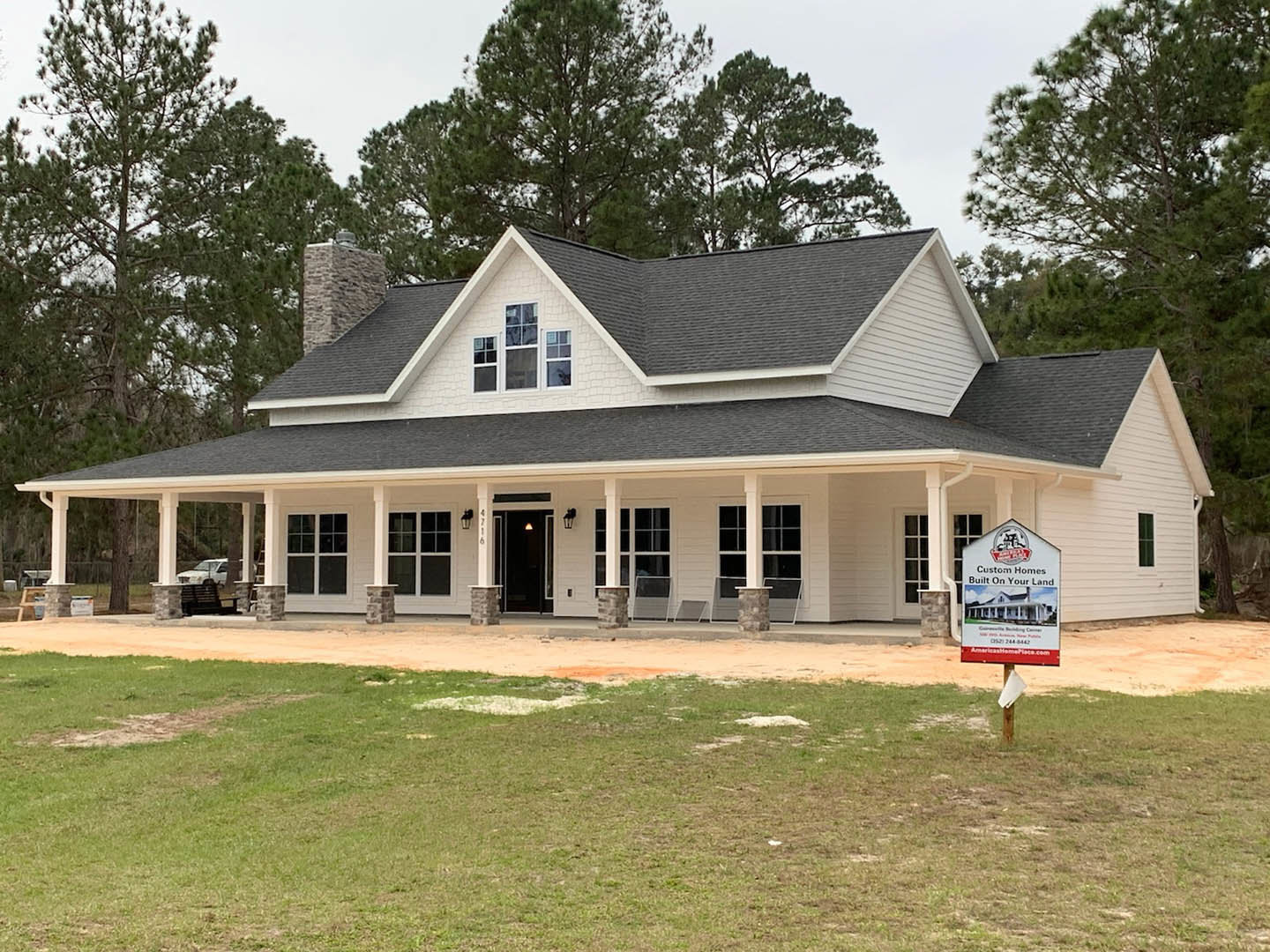 Spacious front porch with white columns, large sign on lawn, black front door with light fixture, windows flanking entry, grassy yard, white car parked on driveway