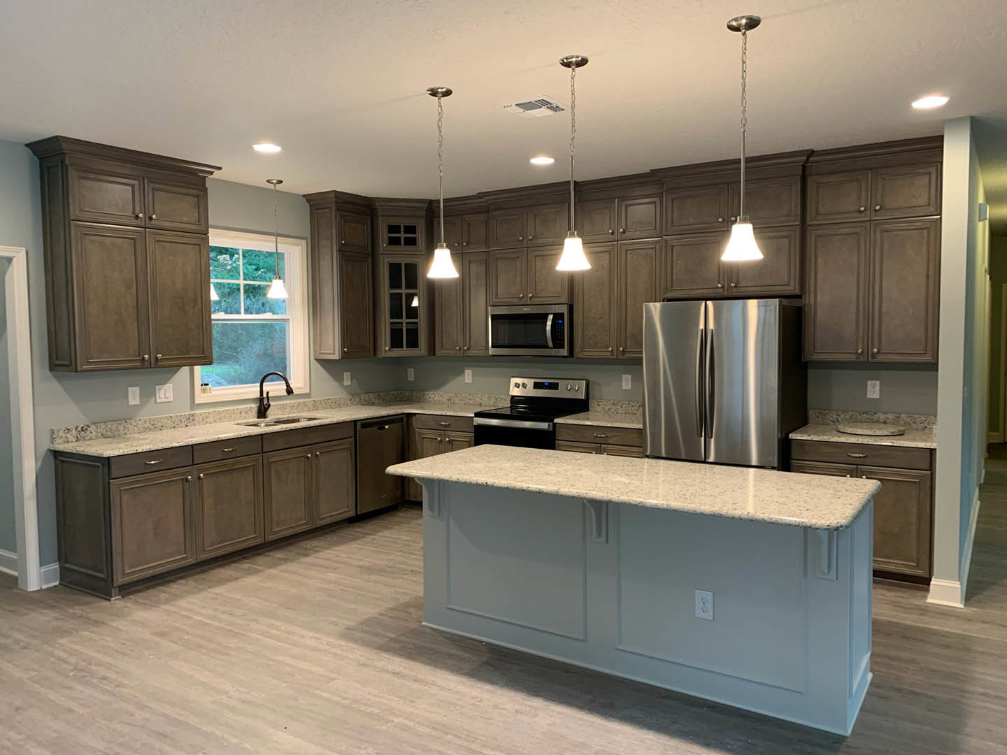 Kitchen with a large white island countertop, stainless steel refrigerator, black curved faucet, tile backsplash, white cabinetry, and hardwood flooring