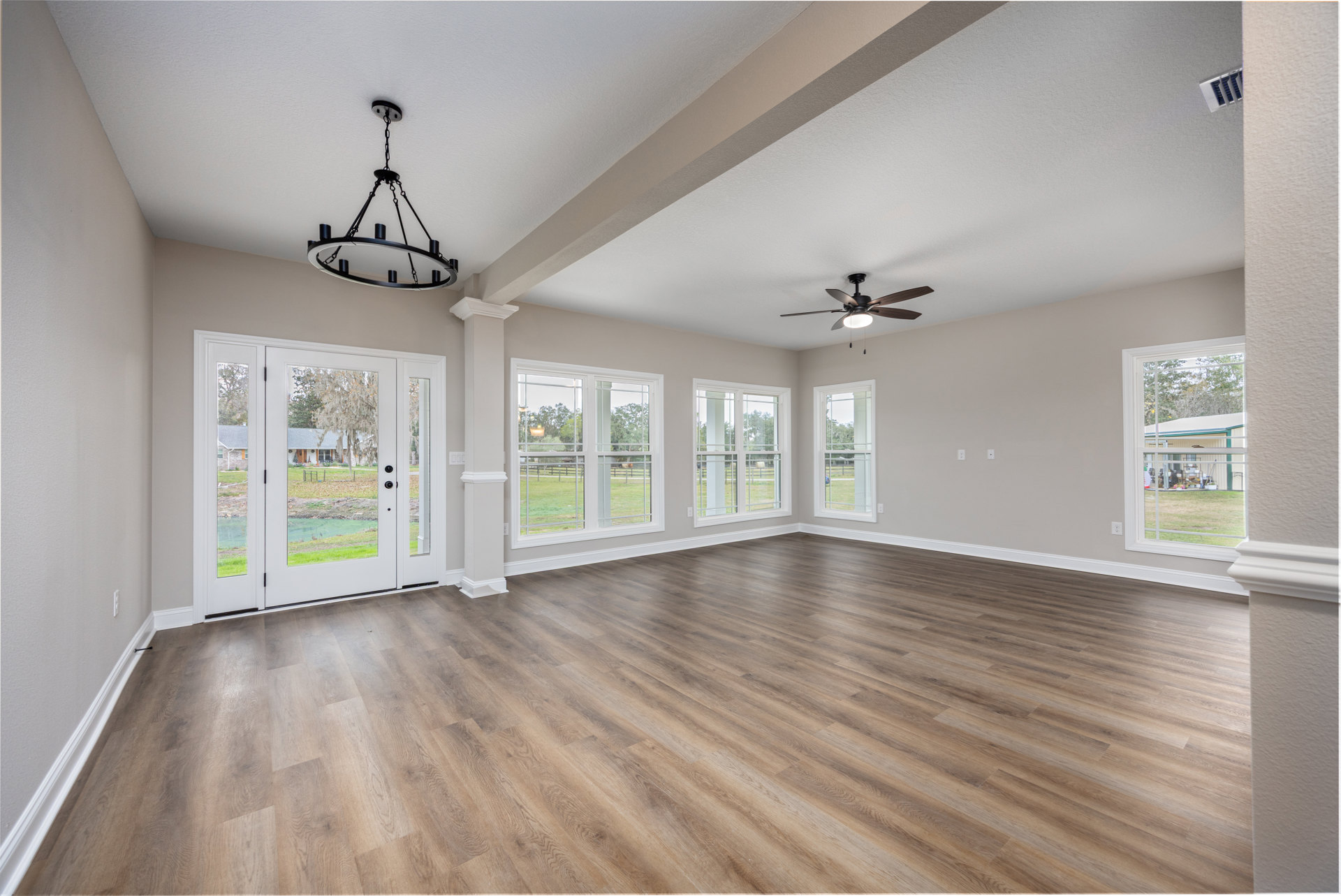 Hardwood flooring, black chandelier, ceiling fan with light, double glass-paneled doors, window overlooking grassy field, white plaster walls
