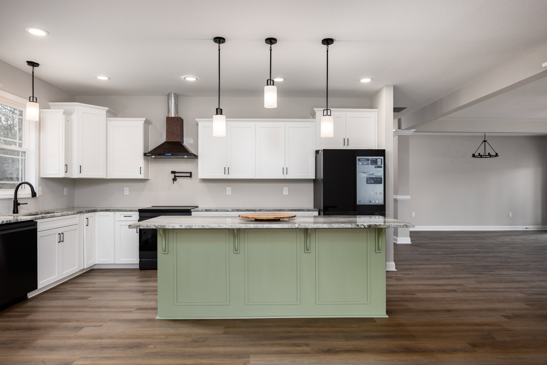 Spacious kitchen featuring a large central island with light stone countertop, round wooden cutting board, black refrigerator with digital screen, white pendant light with black