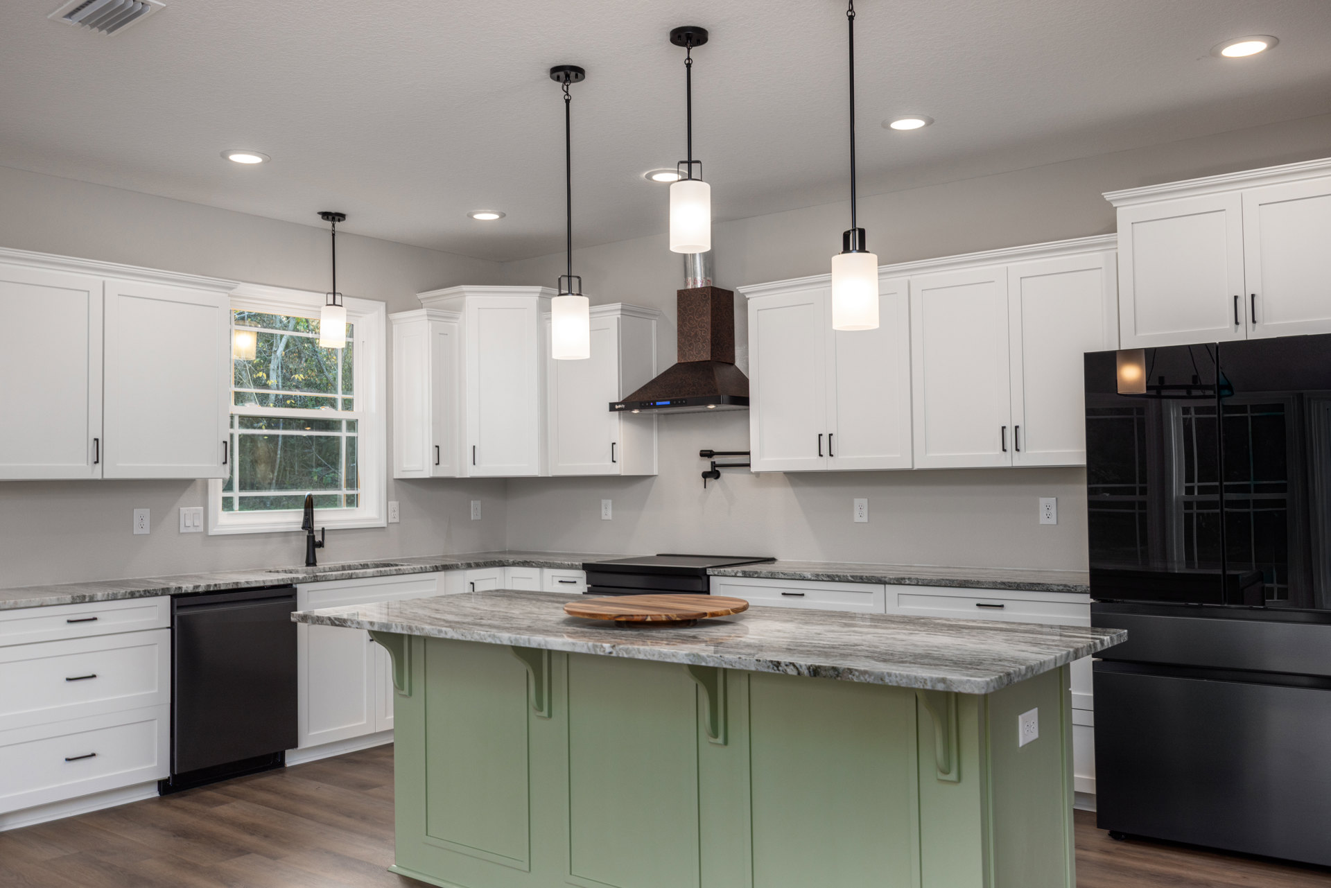 Spacious kitchen featuring a large central island with marble countertop, black cabinetry, wood cutting board, stainless appliances, and pendant lighting against white walls.