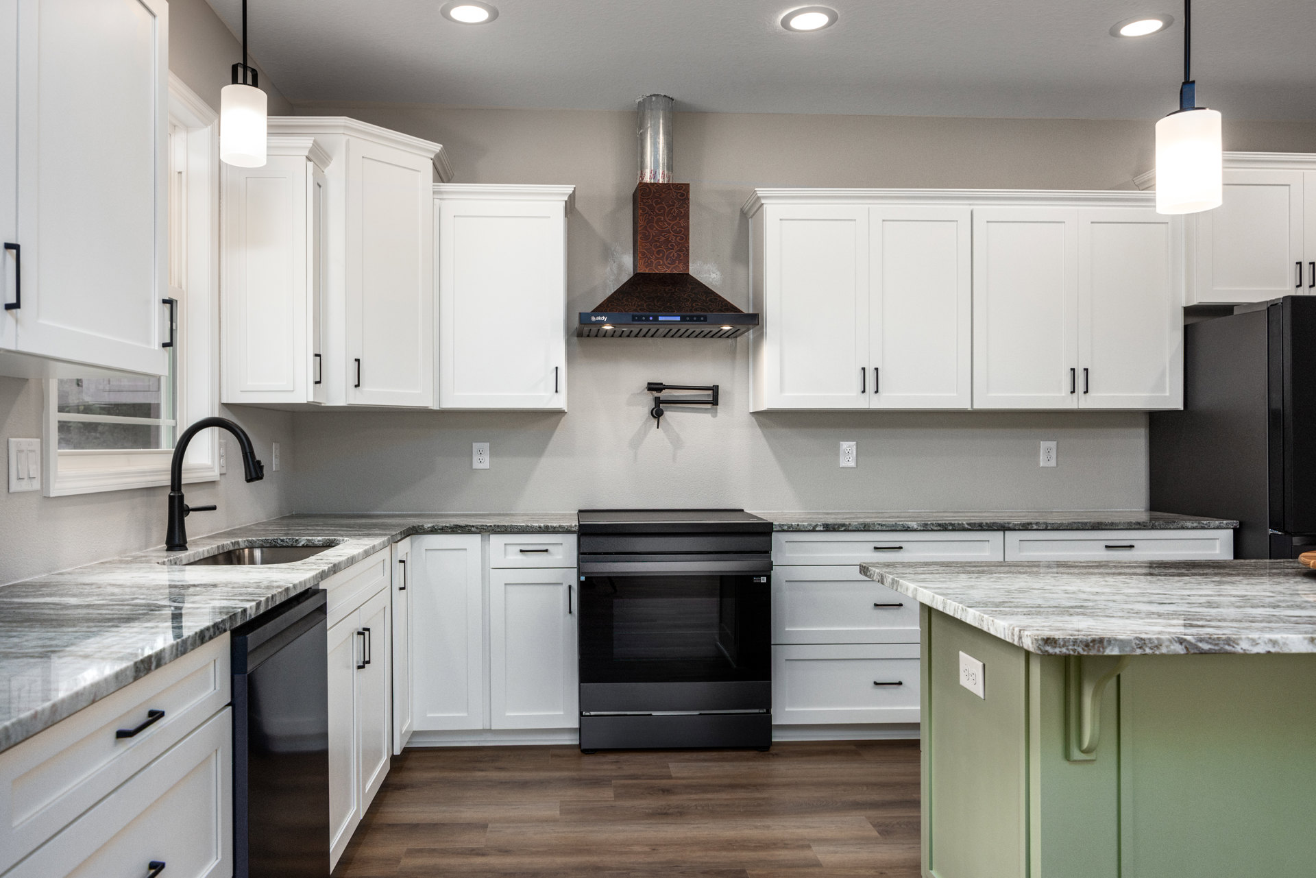 White kitchen cabinets, black appliances including a glass-door oven, marble countertop, black faucet beneath a white-trimmed window, pendant light fixture, exposed metal ductwork