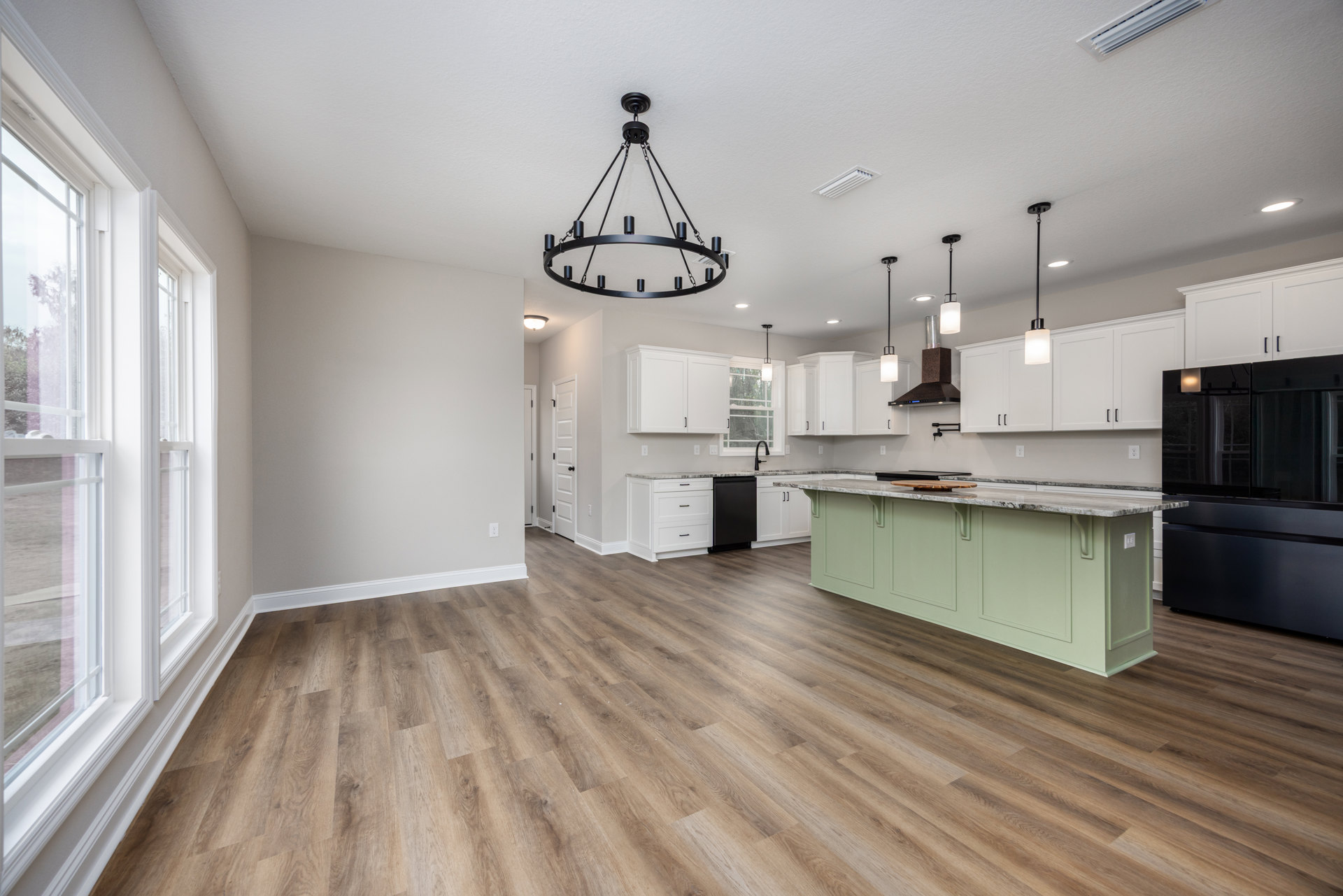 Kitchen with white cabinets, wood flooring, black chandelier with candle-style lights, black television on countertop, white window frame and trim