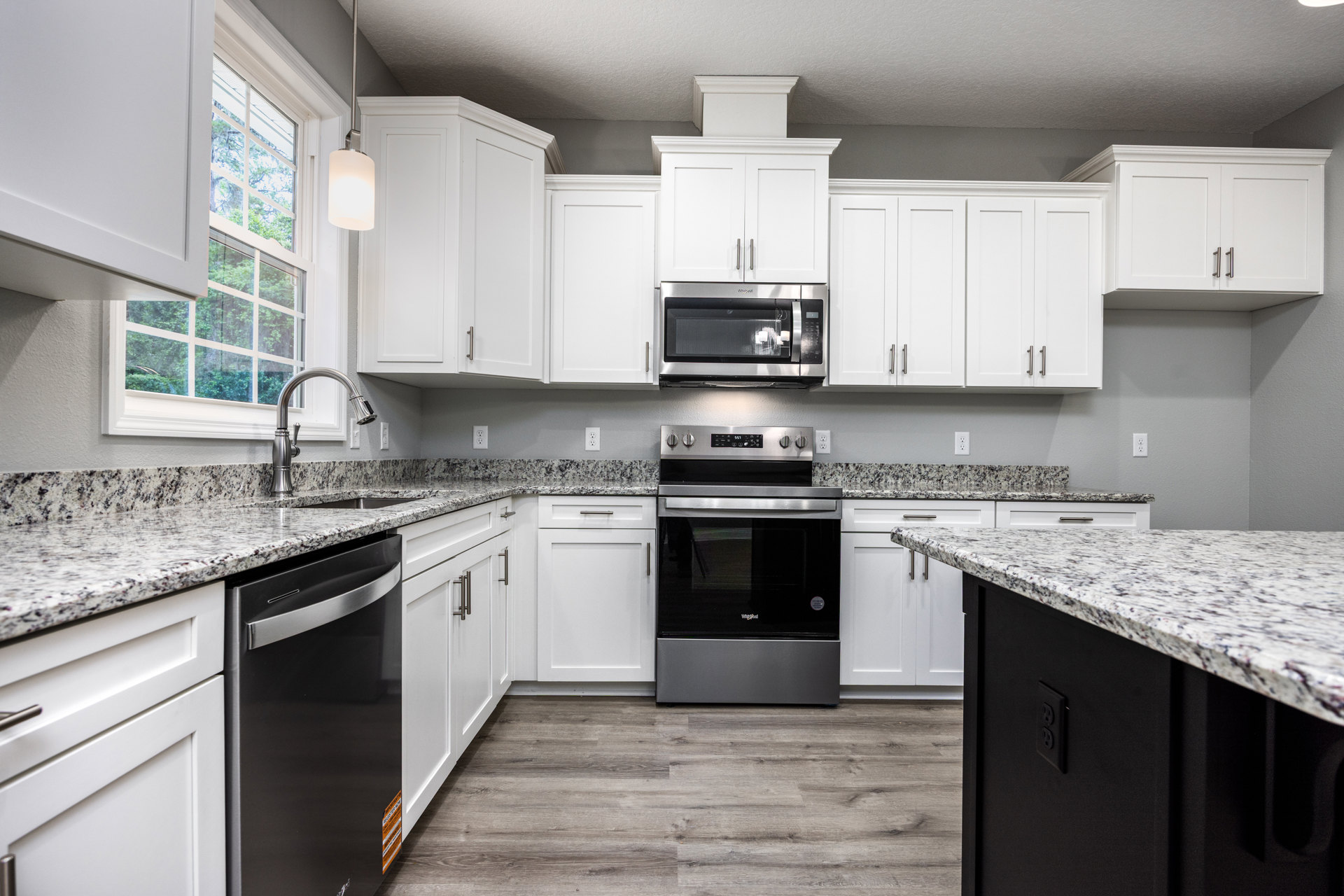 White kitchen cabinets and granite countertops, black and silver oven, close-up microwave, black dishwasher with silver handle, kitchen island with marble countertop, wall-mounted