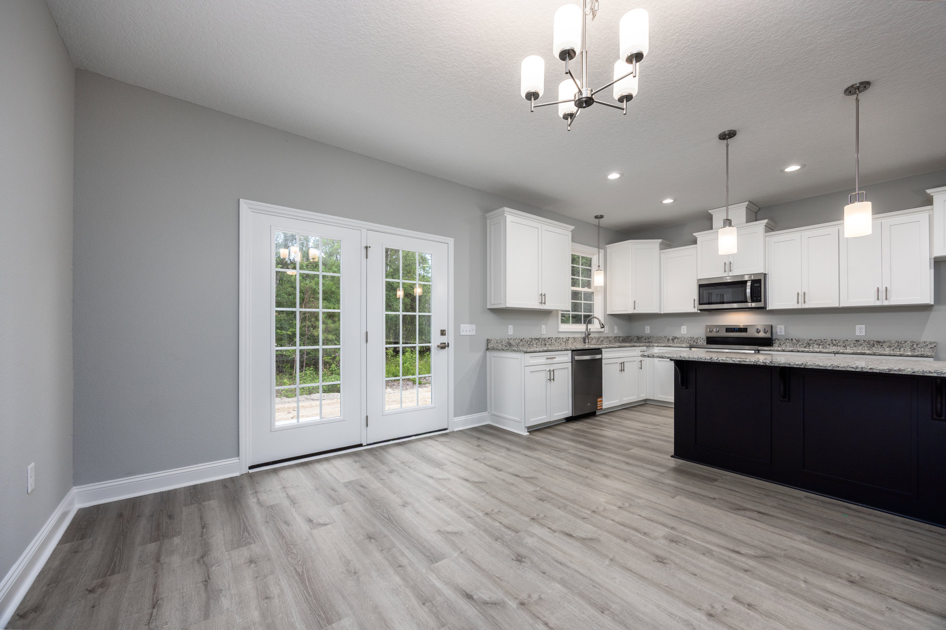 Open kitchen and dining area featuring white cabinetry, wood flooring, built-in microwave, glass double doors, large window with outdoor trees, and white glass shade light fixture.