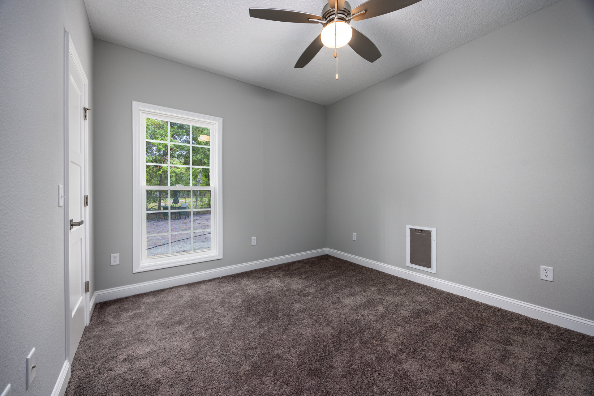 Carpeted room with white plaster walls, ceiling fan with light fixture, large window overlooking backyard, close-up of paneled door