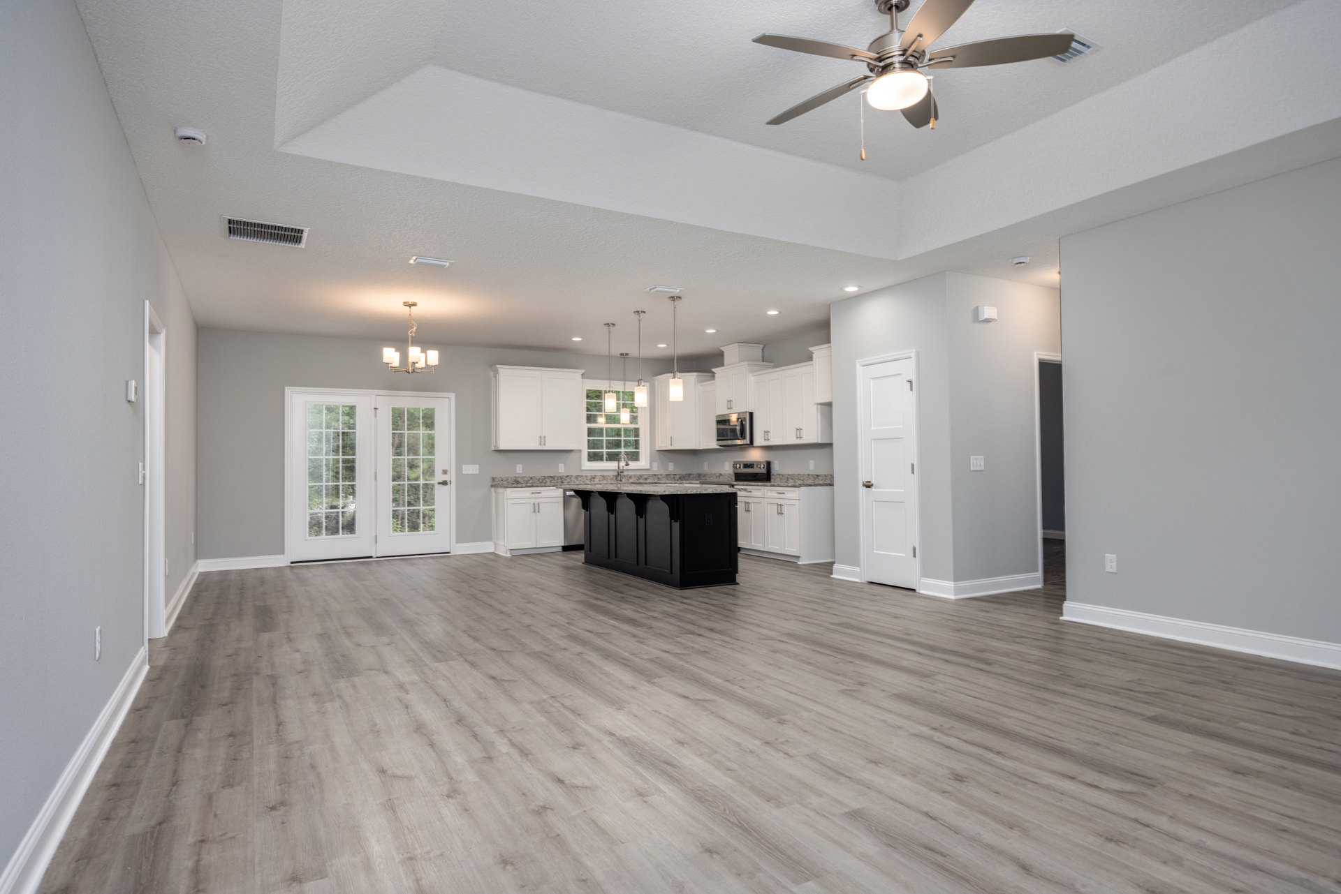 Spacious kitchen with black cabinets, marble countertop island, laminate flooring, ceiling fan with light, double glass-paneled doors, and white door with silver handle
