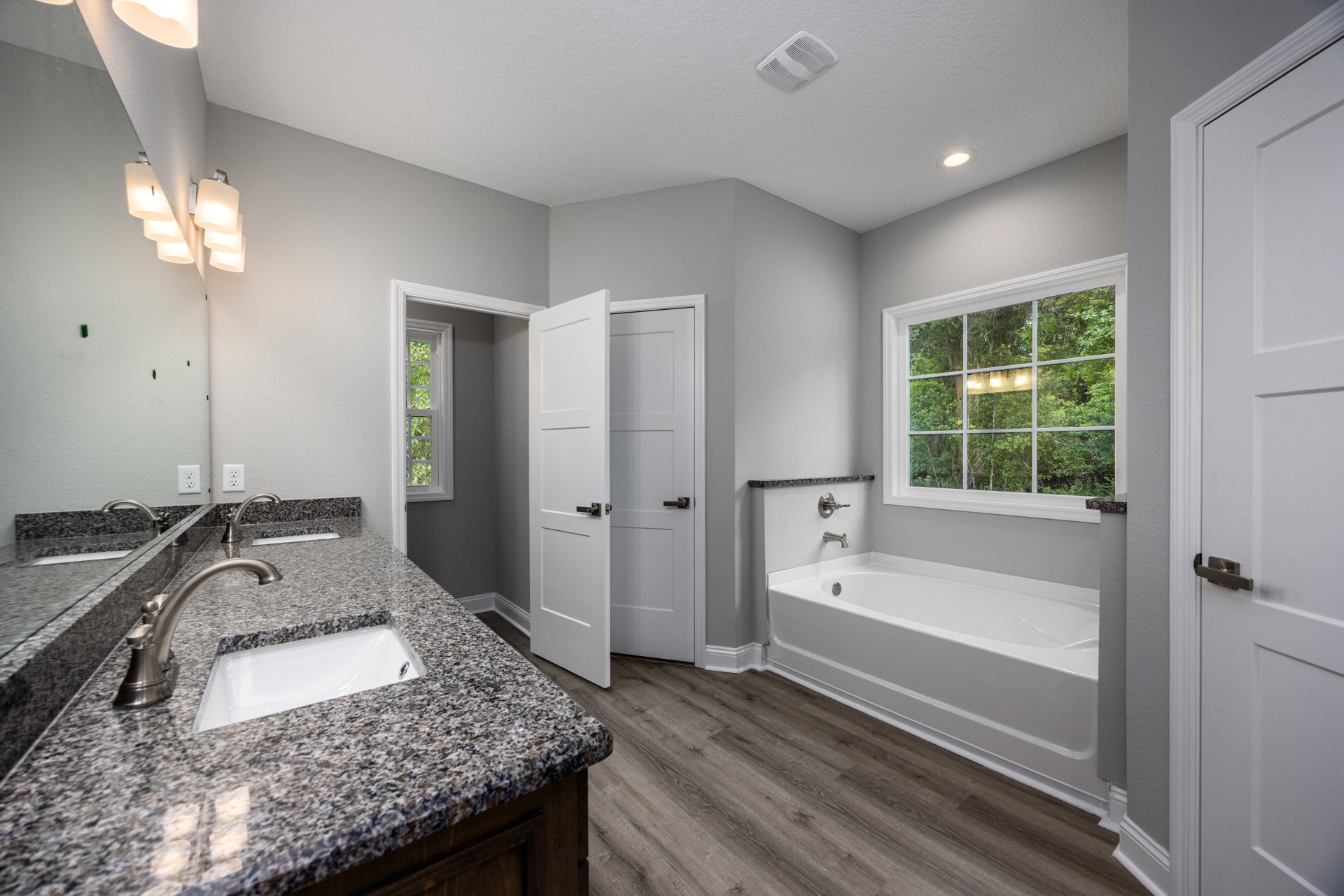 Marble countertop with undermount sink and chrome faucet in a bathroom, white tile backsplash, window with view of trees, white door with silver doorknob