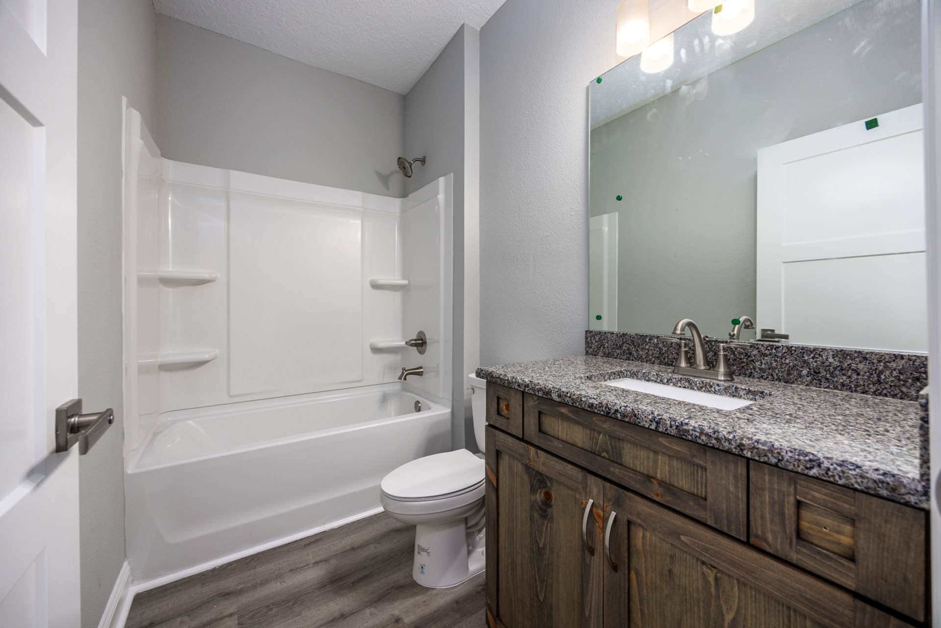 White porcelain sink set in a light stone countertop with dark wood cabinetry, matching white toilet, large wall mirror, and neutral tile flooring in a modern bathroom.