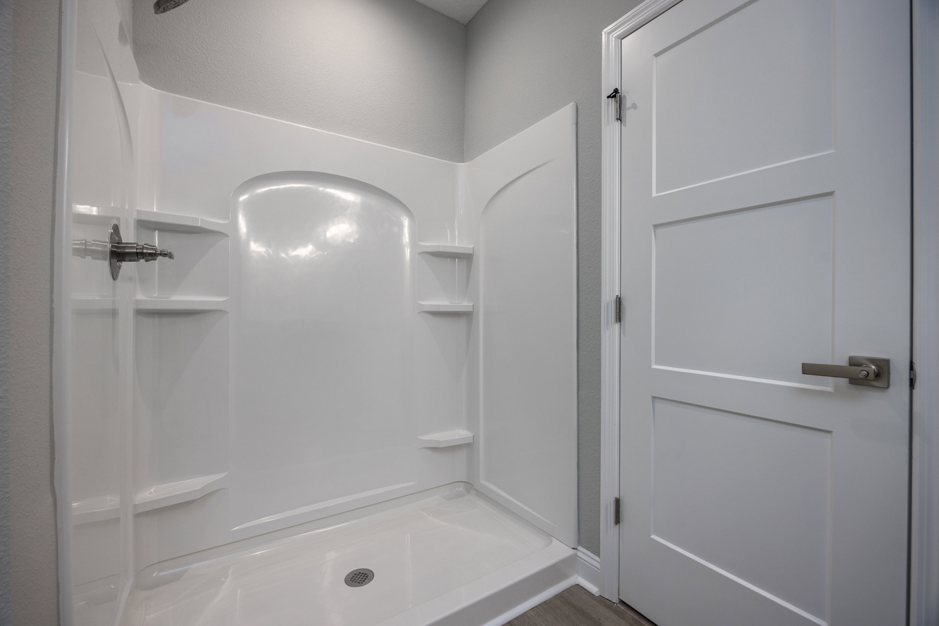 White tile shower with built-in shelves, glass door with silver handle, wall-mounted shower head, and floor drain