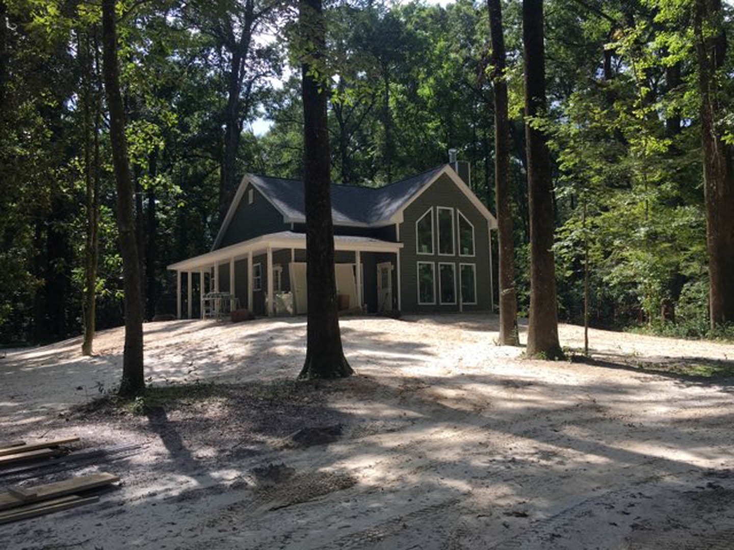 Modern wood-clad home with covered porch nestled among tall trees, snow covering ground and stacked firewood near entrance
