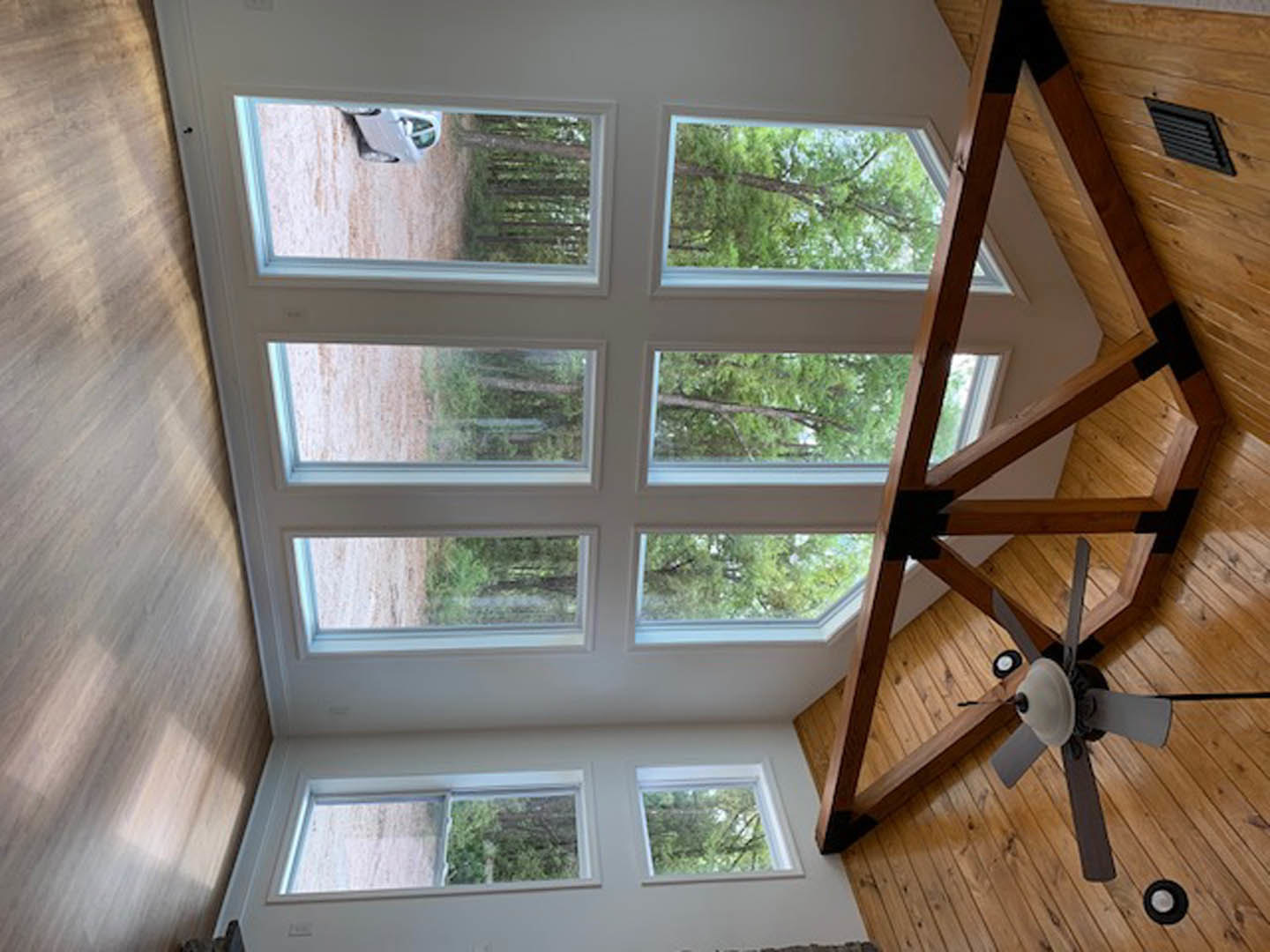 Ceiling fan mounted on white ceiling above hardwood floor, large windows with multiple panes lining one wall, wooden table positioned near windows, natural light illuminating room