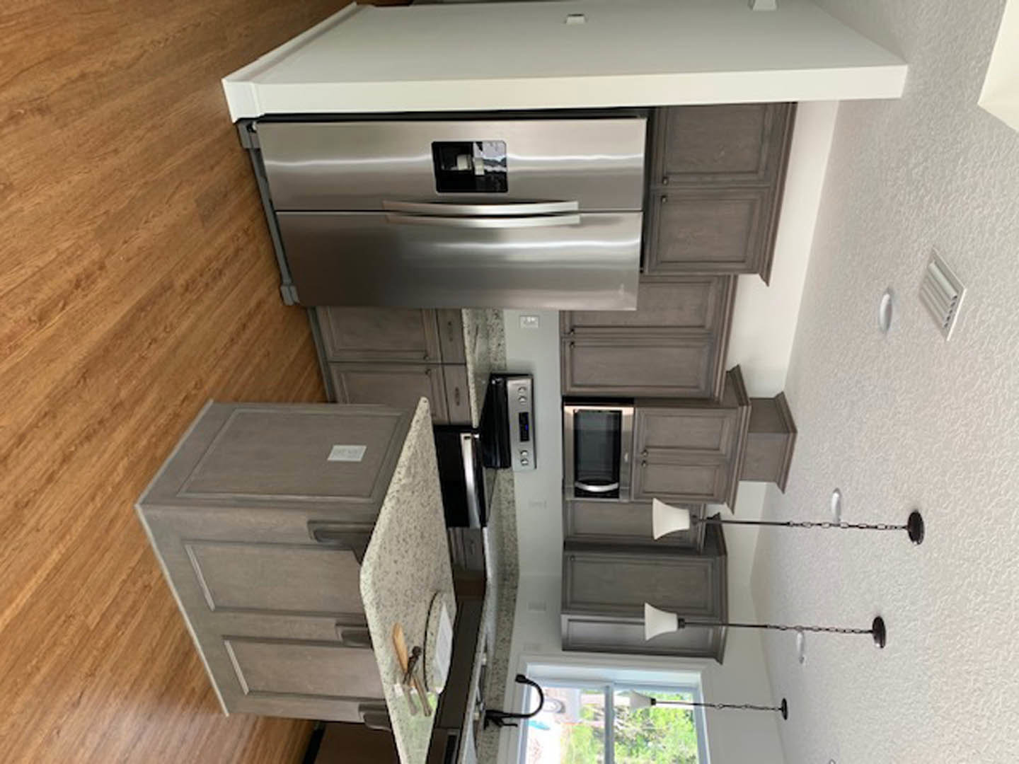 Modern kitchen featuring a stainless steel refrigerator, wood cabinetry with silver handles, light-colored ceiling, and a dining table on hardwood flooring