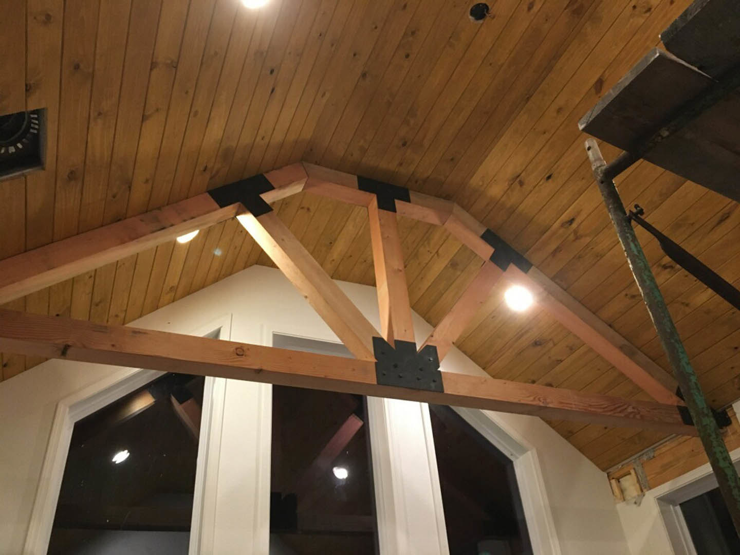 Exposed wooden ceiling beam with natural hardwood finish spanning across a bright indoor room with white walls and metal fixtures.