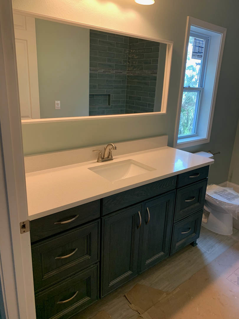 Modern bathroom with rectangular mirror above white sink and chrome faucet, light-colored countertop, white toilet partially wrapped in plastic, window with temporary sign, neutral