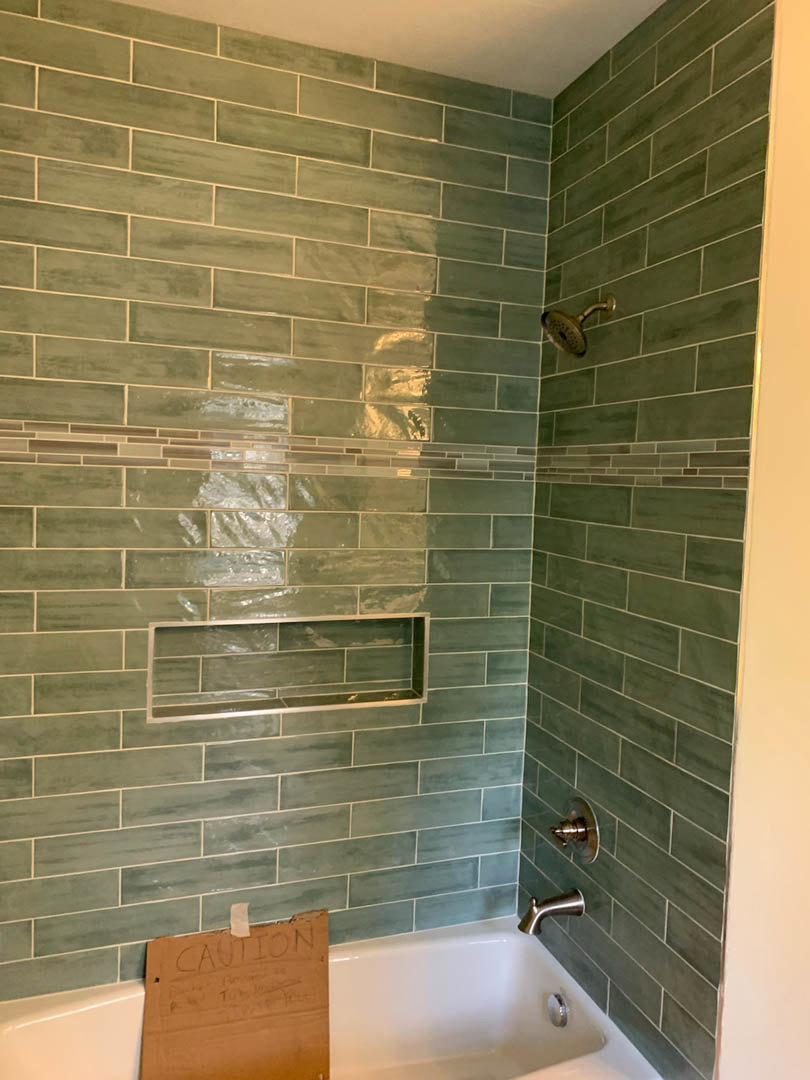 Walk-in shower featuring a tile wall, chrome shower head, built-in tile shelf, and modern faucet