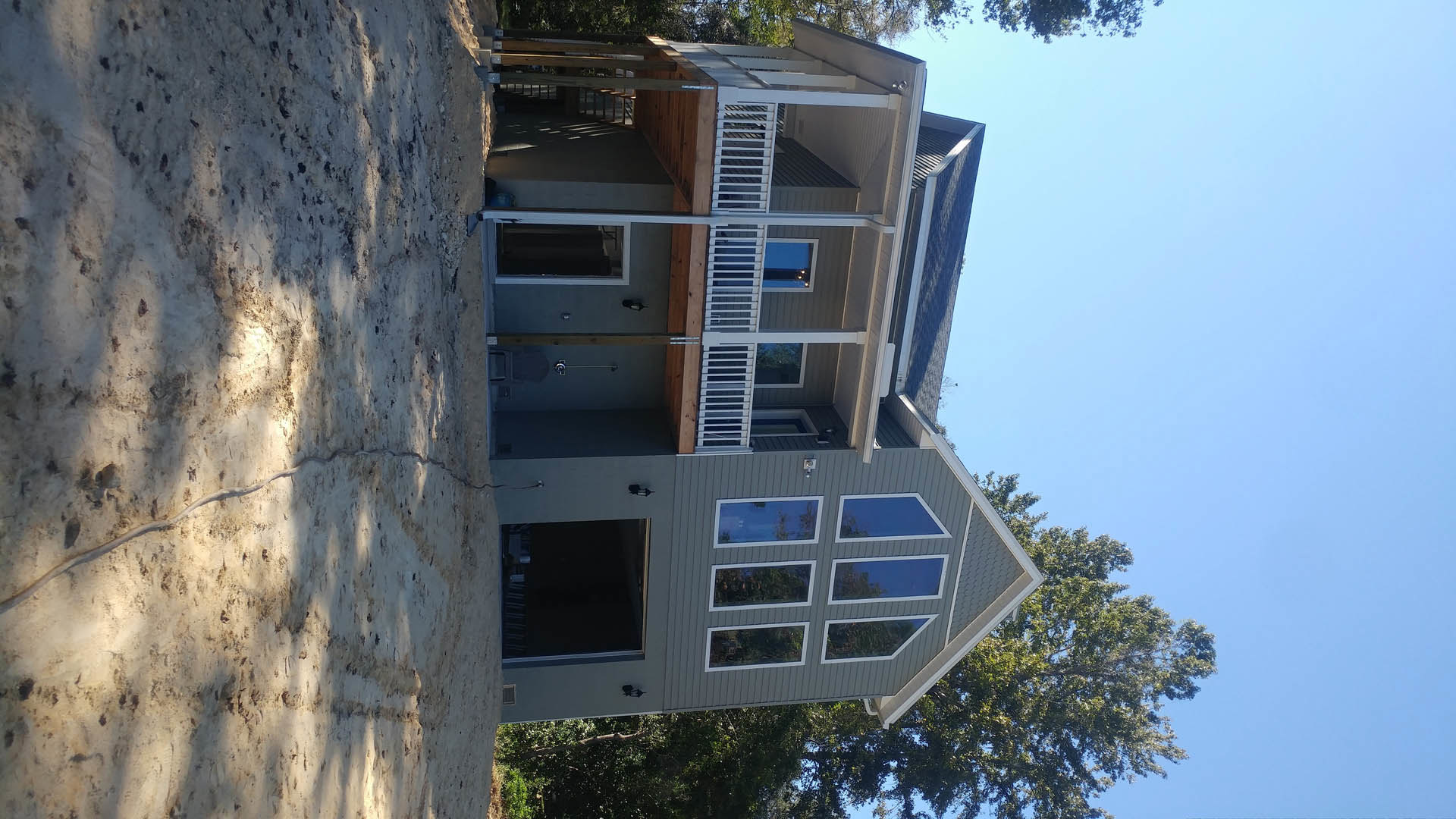 Two-story house with white siding, large front porch, multiple windows, and mature tree in landscaped yard