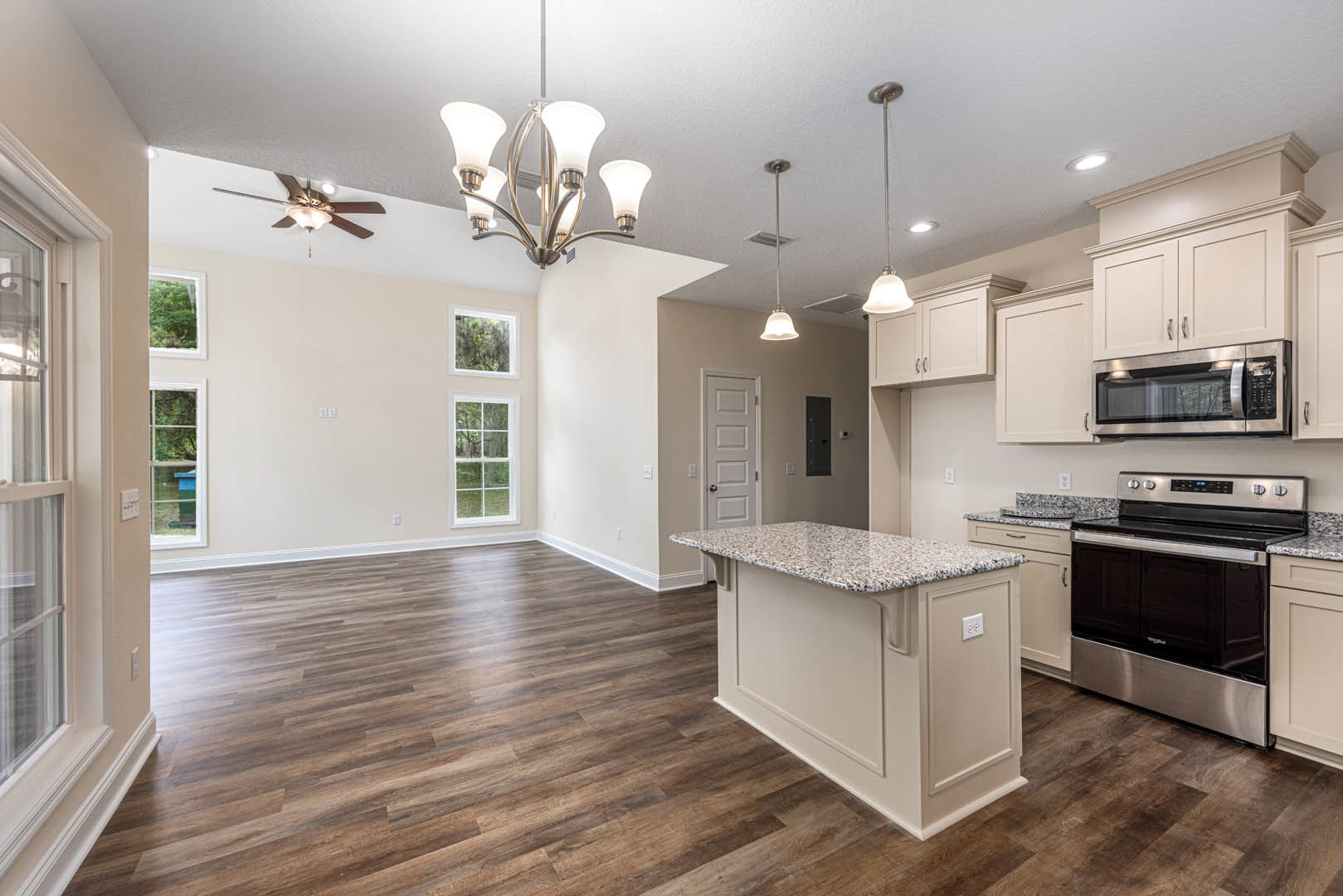 Open-concept kitchen and living room featuring hardwood floors, white cabinetry, stainless steel microwave and stove, granite kitchen island, and modern five-light fixture.