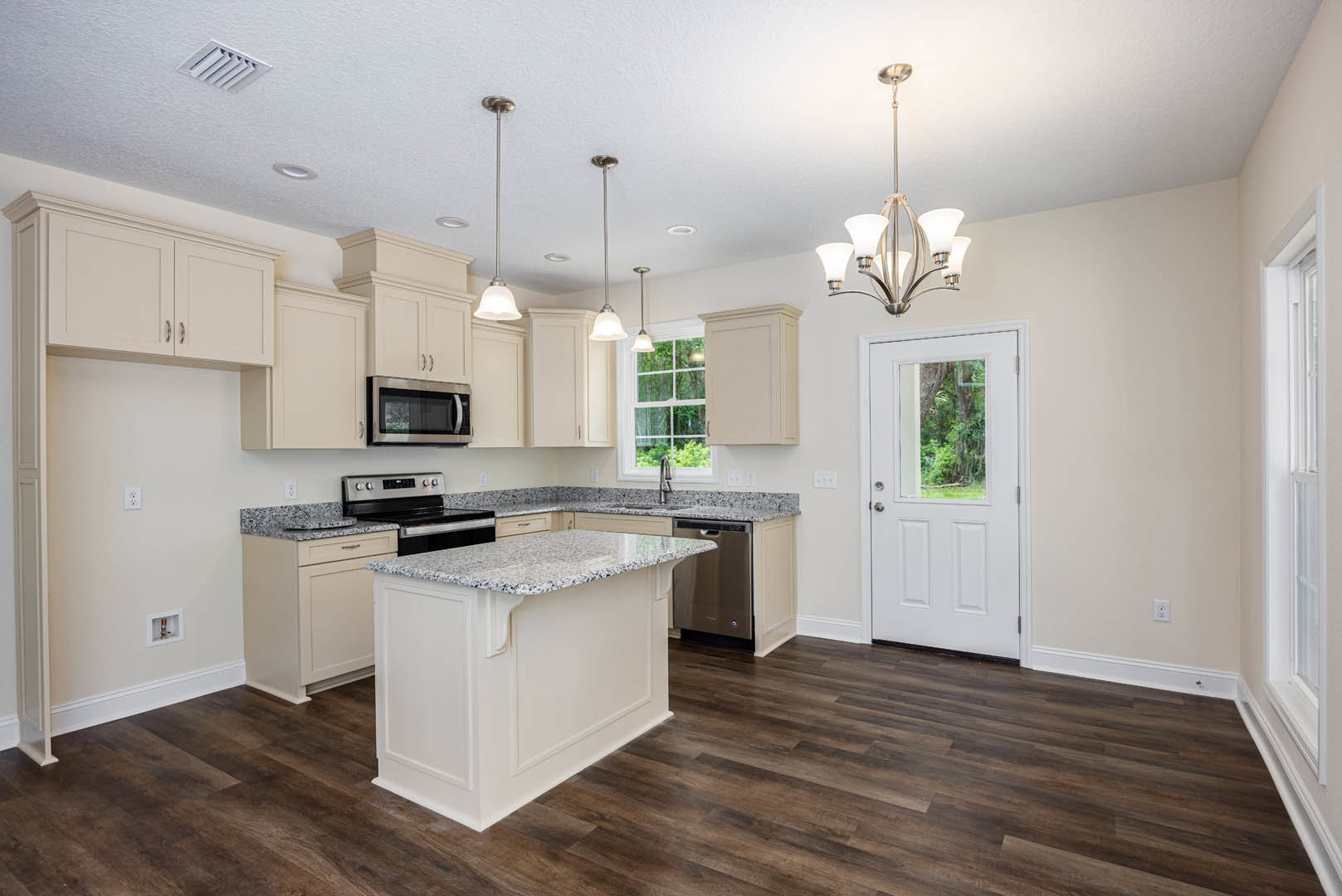 Marble kitchen island with waterfall edge, wood plank flooring, white cabinetry, stainless steel microwave, glass-paneled door, modern chandelier overhead