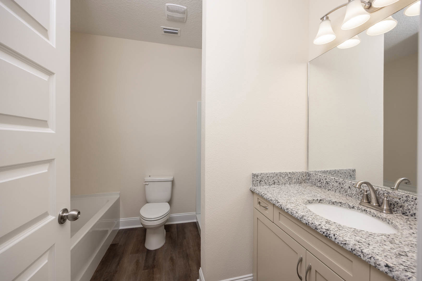 Bathroom with marble countertop, undermount sink, wall-mounted mirror, white toilet, tile flooring, and modern light fixture