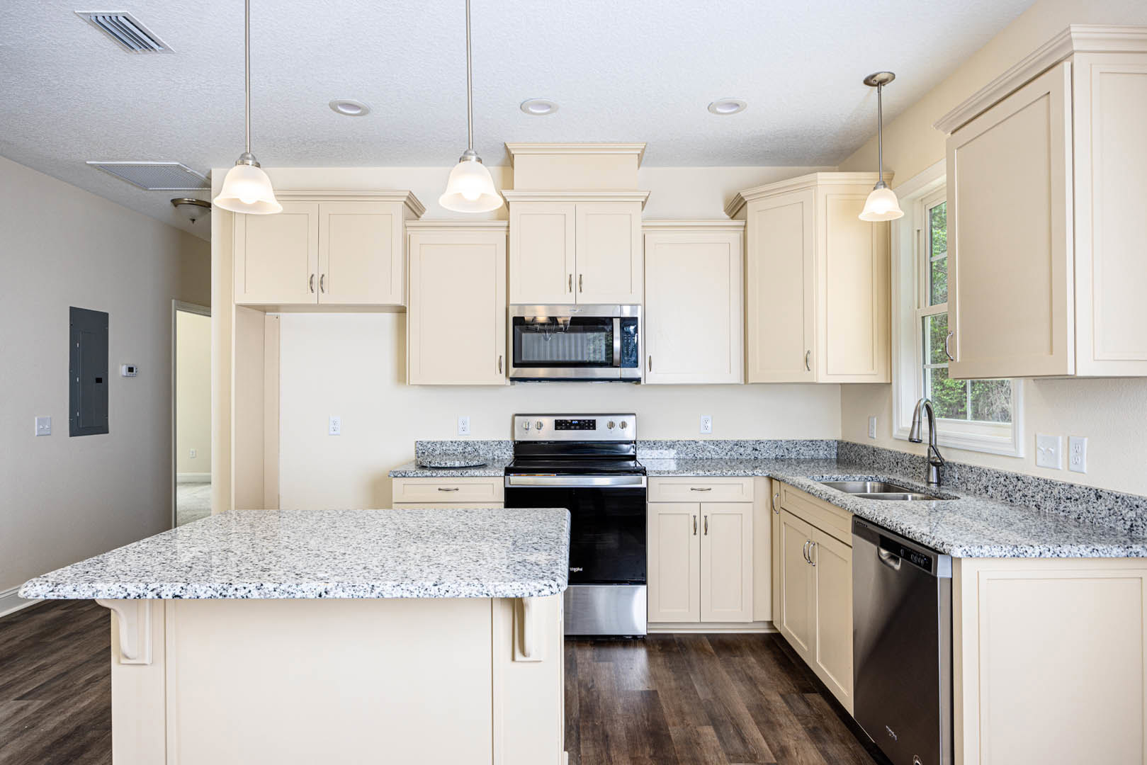 Granite countertops with black speckled finish, stainless steel stove and microwave, white cabinetry, built-in sink, and modern appliances in a custom kitchen