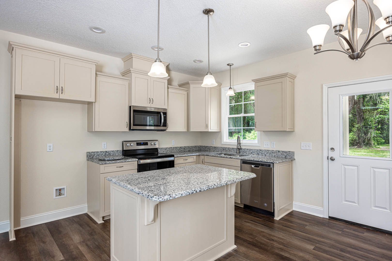 Granite countertops, stainless steel dishwasher, kitchen island, white cabinetry, built-in microwave and oven, chandelier, white door with window, tree visible outside