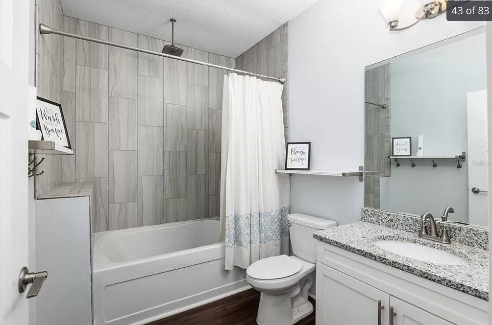 Bathroom with white shower curtain, white sink with chrome faucet, toilet, light tile flooring, and wall-mounted mirror