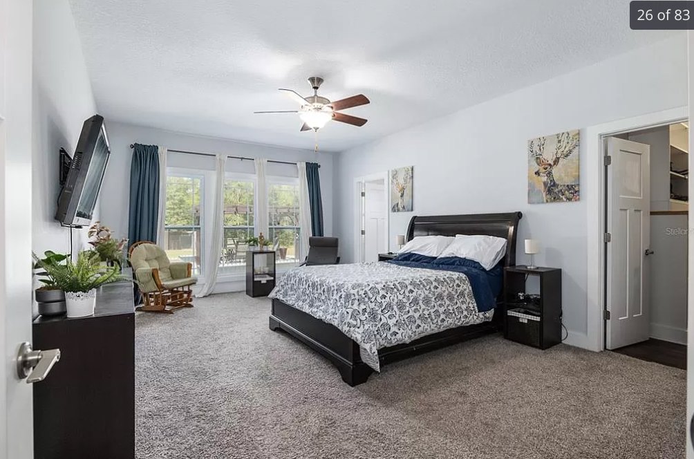 Bedroom with a bed featuring a black and white blanket, ceiling fan with light fixture, wooden rocking chair, neutral walls, and hardwood flooring