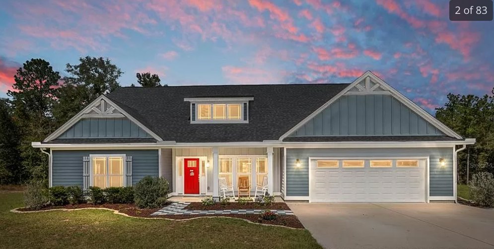 Two-story home with white siding, red front door, attached white garage with two windows, concrete driveway, small porch, and pink clouds in the evening sky