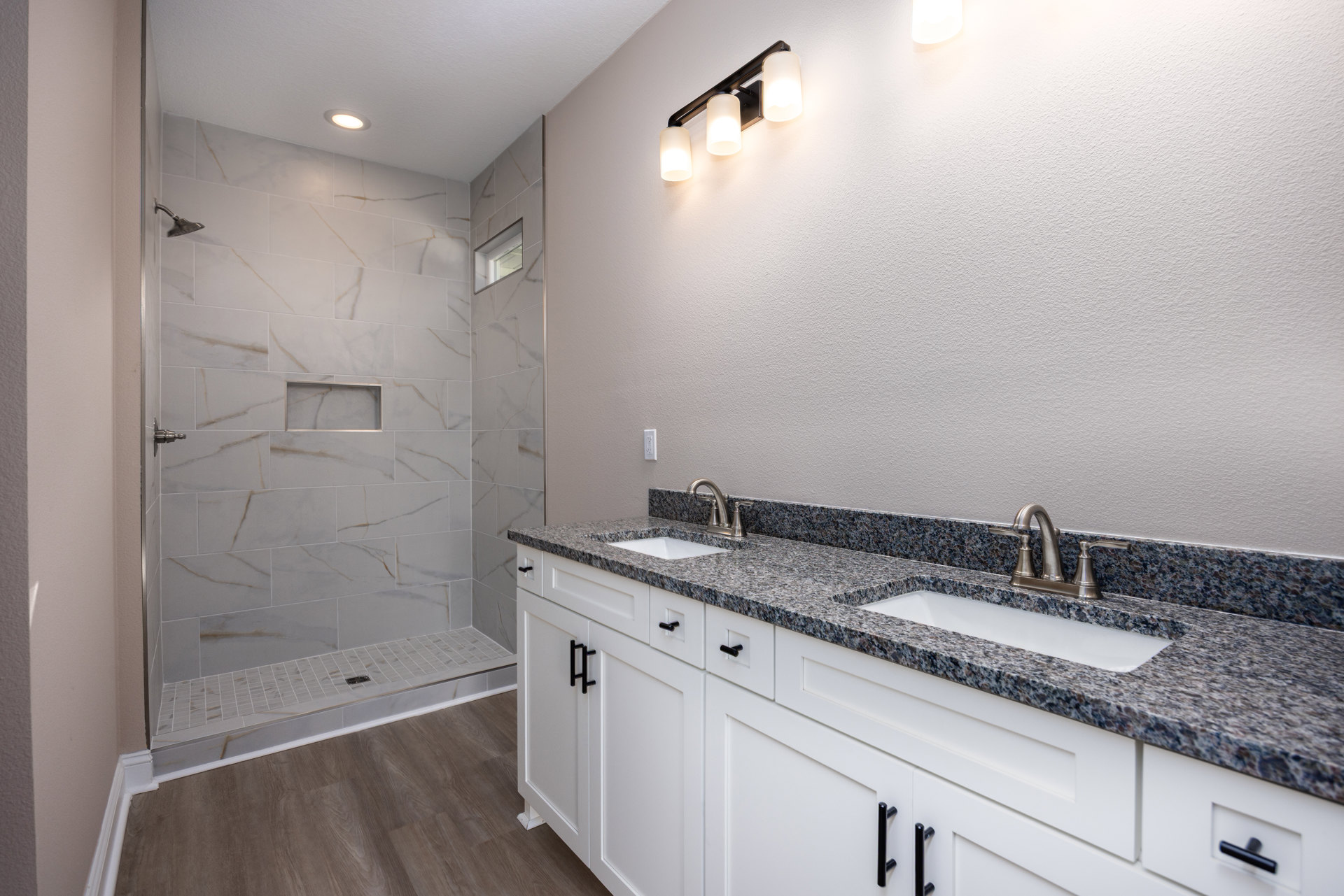 Bathroom featuring marble countertops, undermount sink, tile shower enclosure, modern light fixture, and white cabinetry