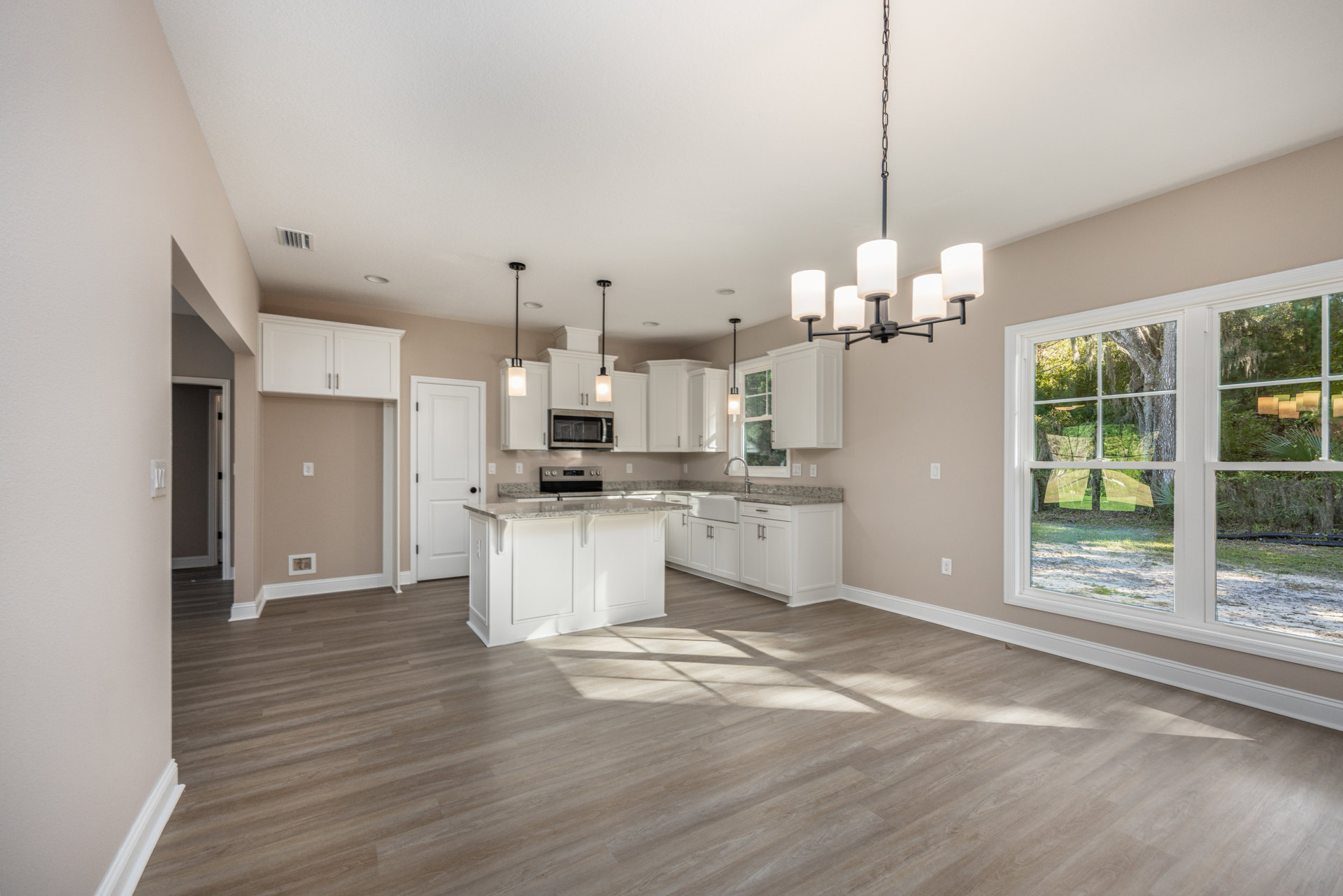 Open-concept kitchen and dining area featuring wood flooring, white cabinetry, open microwave door, black-handled white door, and large window with outdoor view