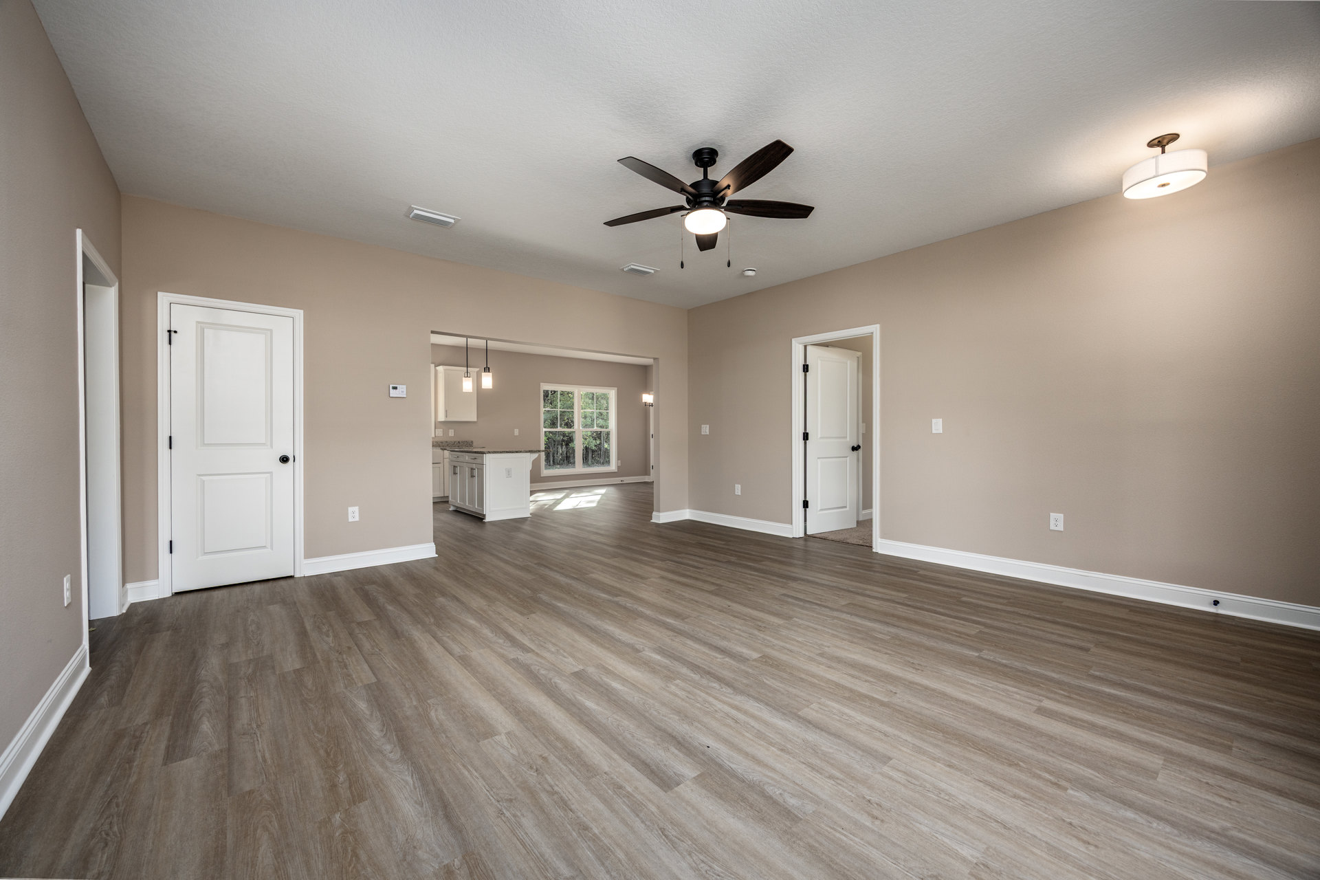 Spacious room with hardwood flooring, white walls, ceiling fan with light, white doors featuring black knobs, and a window overlooking trees