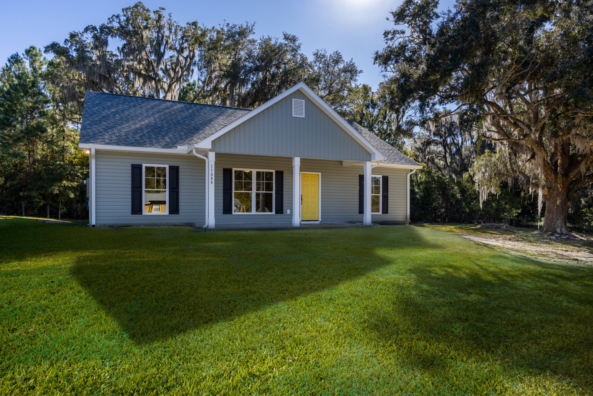 Two-story home with white siding, yellow front door, black handle, white-framed windows with black shutters, front lawn, mature trees, and Little White House visible in the