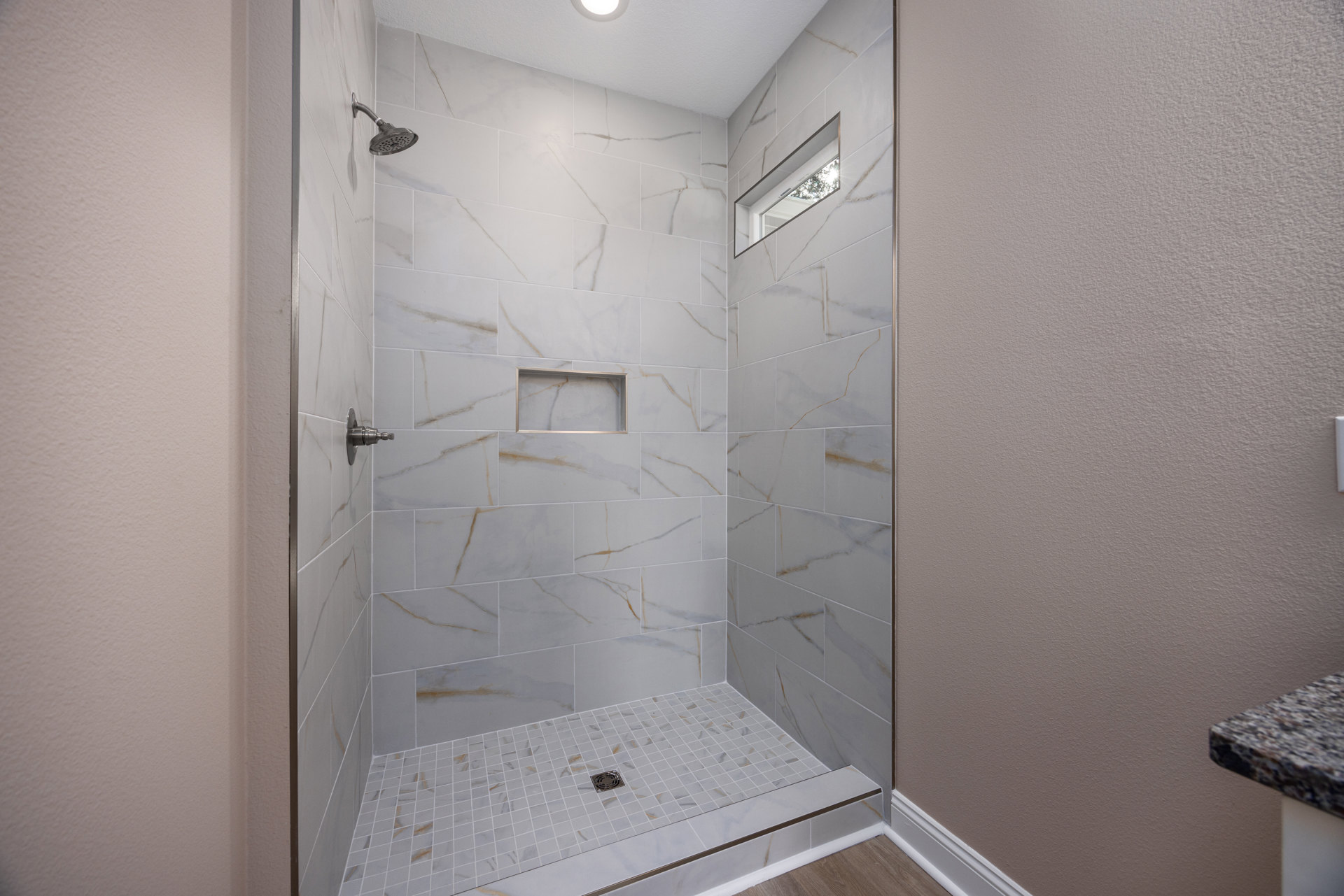 Walk-in shower with white tile walls, silver shower head, marble tile floor, and linear drain