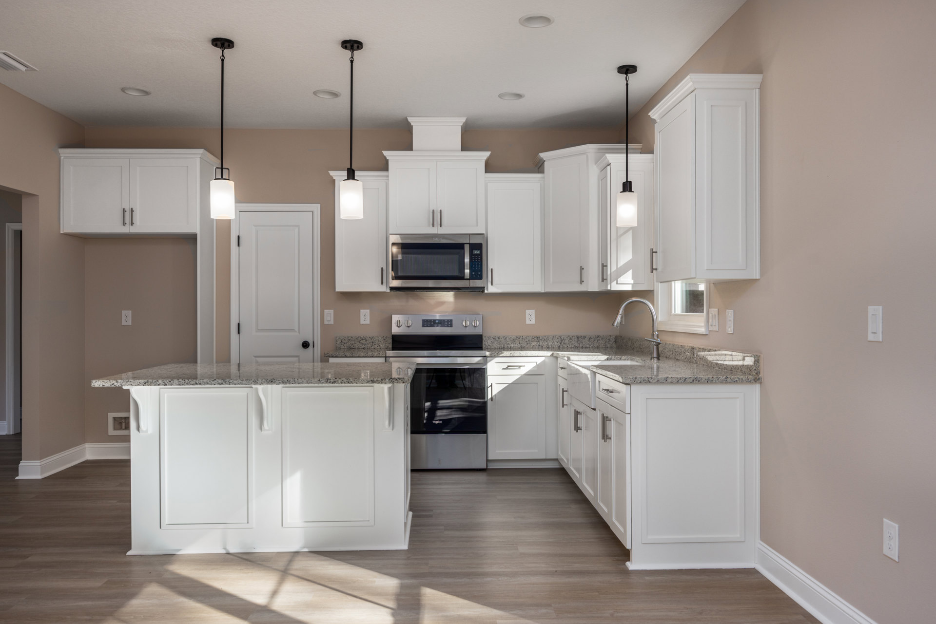 White kitchen cabinets with granite countertops, stainless steel microwave with black door, marble-topped island, white door with black hinges, recessed lighting fixtures