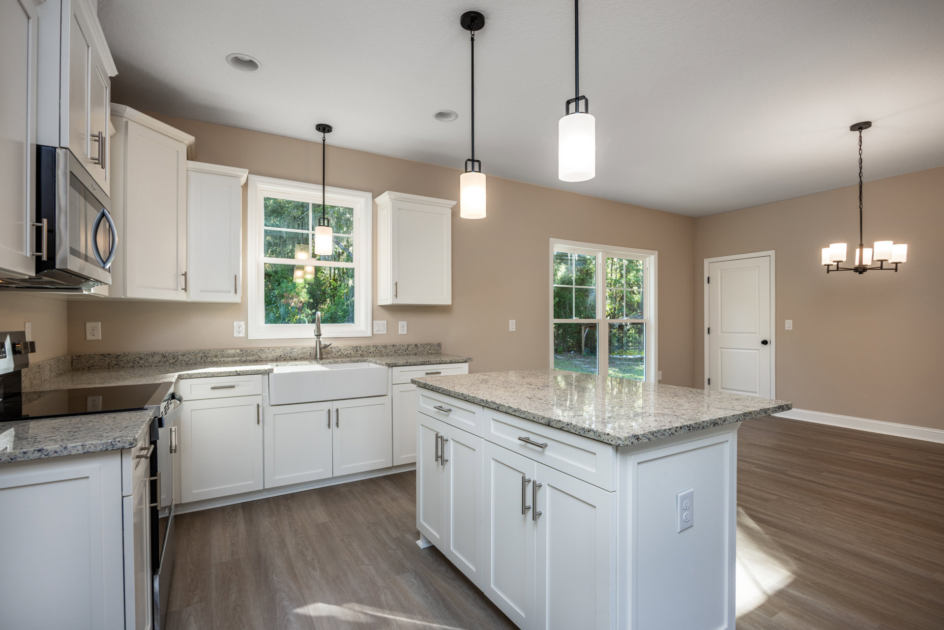Kitchen with white cabinets, granite countertops, stainless steel appliances, kitchen island, white door with black knobs, silver cabinet handles, and a white pendant light hanging