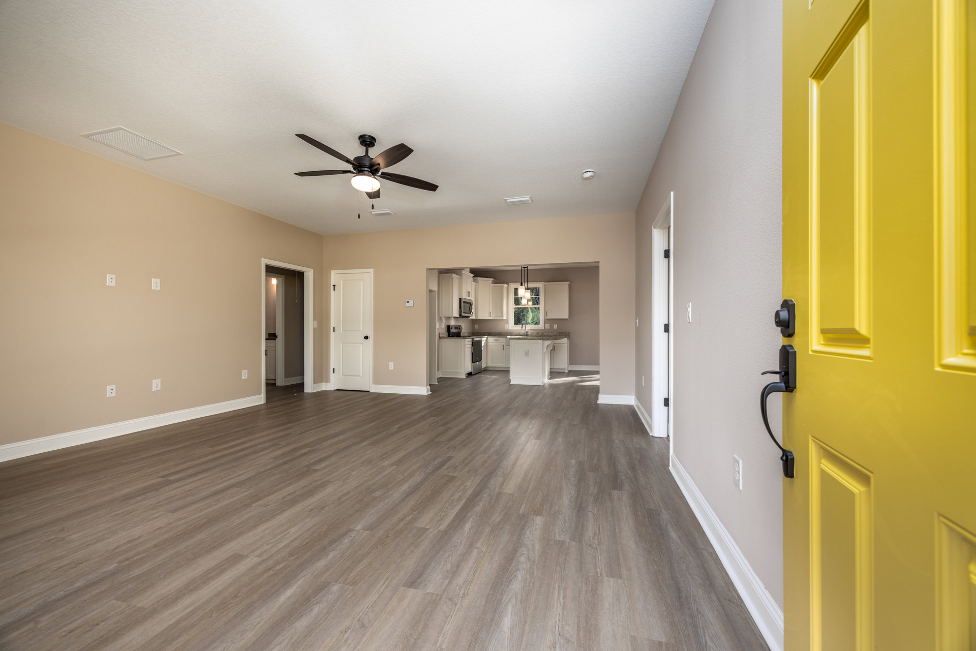 Yellow door with black hardware, wood flooring, white cabinet topped with marble, ceiling fan with light fixture, white walls and trim