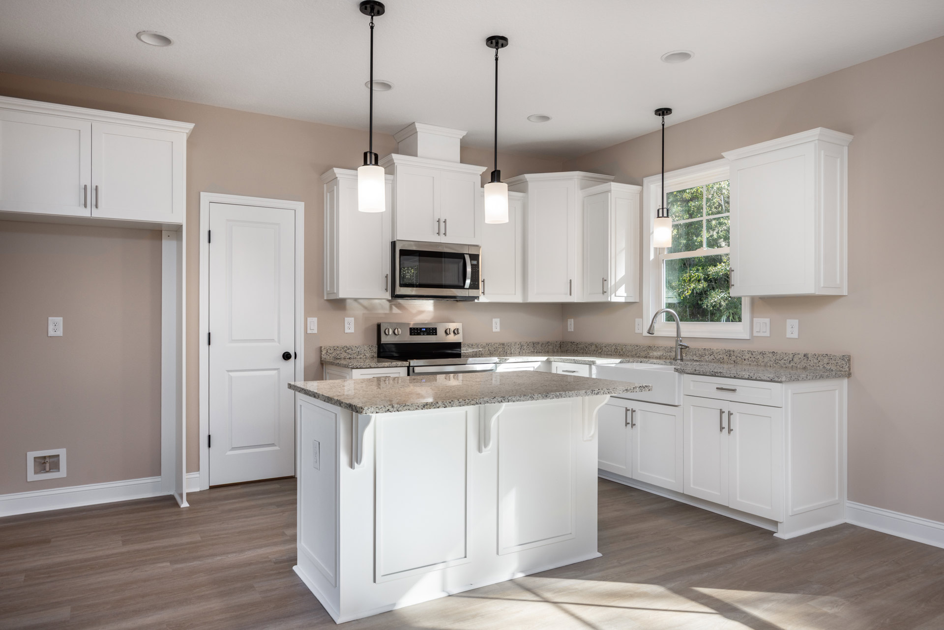 Kitchen featuring white shaker cabinets, marble countertops, open microwave door, granite island, black hardware, and light wood flooring