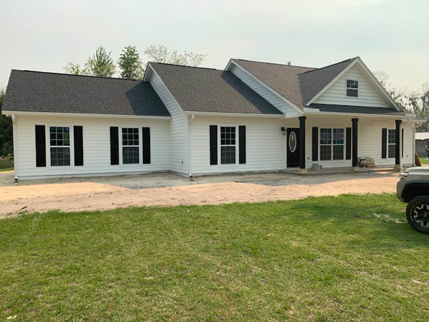 White siding house with black shutters, grassy lawn, Robert Frost Farm visible in the background, blue sky overhead