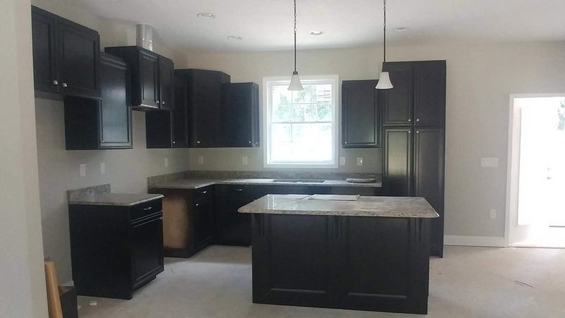 Black kitchen cabinets with marble countertop, white lamp shade on table, black drawer cabinet, white window with light fixture, white rectangular object with black border
