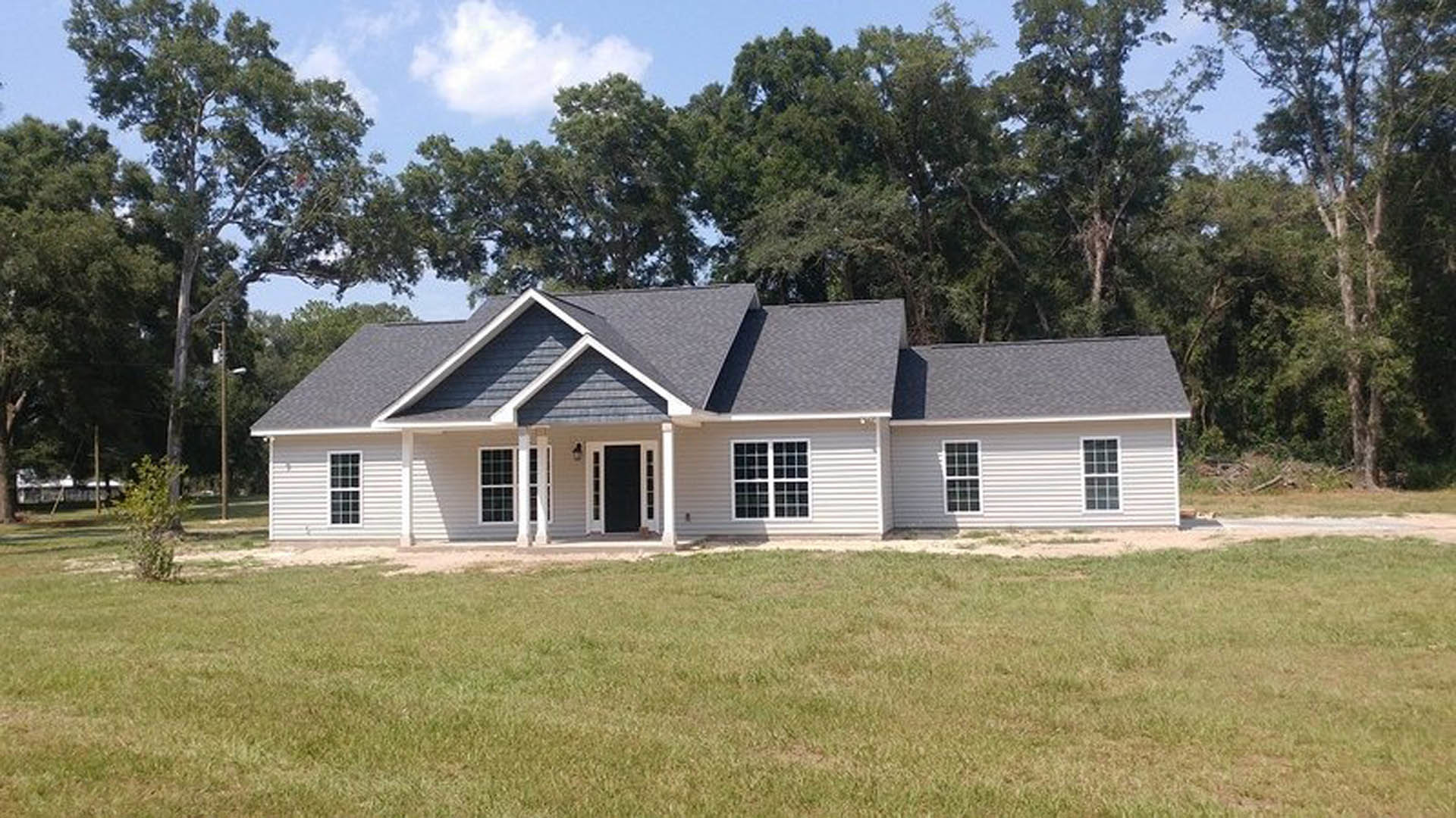 White two-story home with white siding and roof, rectangular windows with white trim, manicured green lawn, mature tree on the right, partly cloudy sky overhead