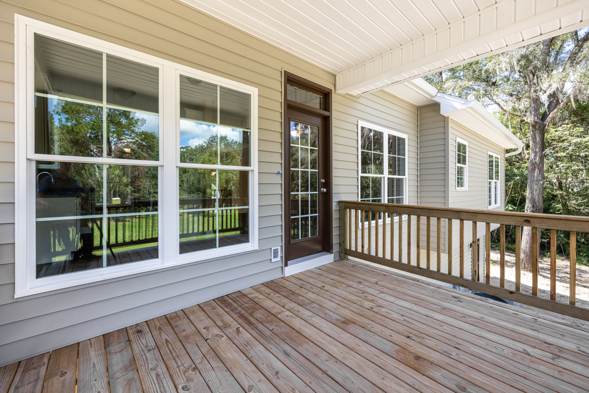 Wooden deck with horizontal railing, white-trimmed window, and glass-paneled door featuring a silver knob, attached to light-colored house exterior