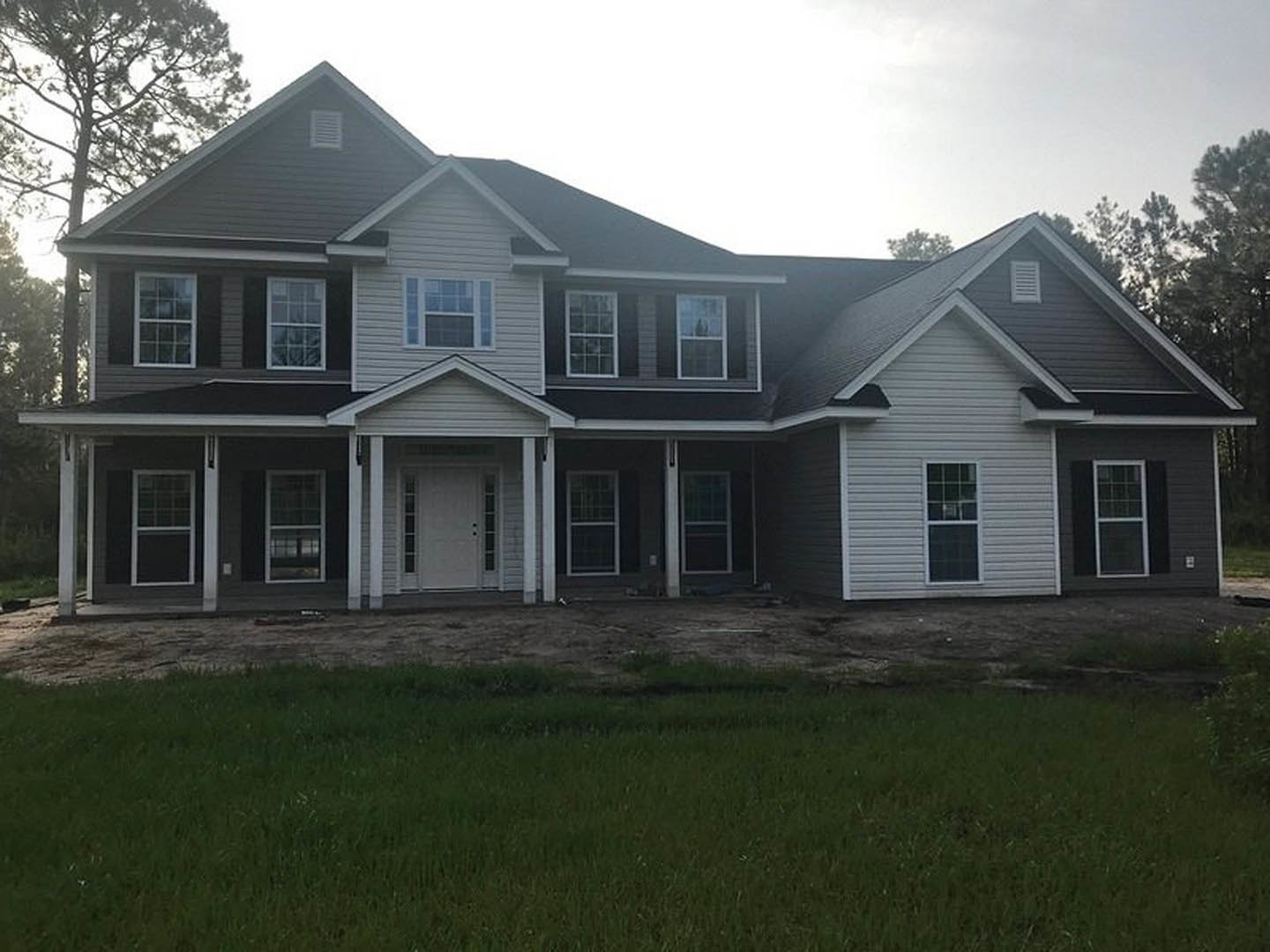 Two-story house with white siding, covered porch, white-framed windows, white front door, manicured lawn, and mature trees in the yard