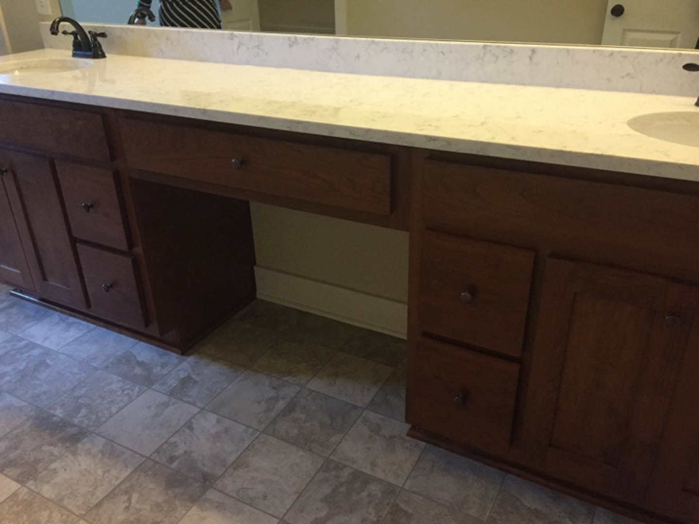 White countertop with chrome faucet, large wall mirror, light-colored tile floor, and sleek cabinetry in a modern bathroom or kitchen.