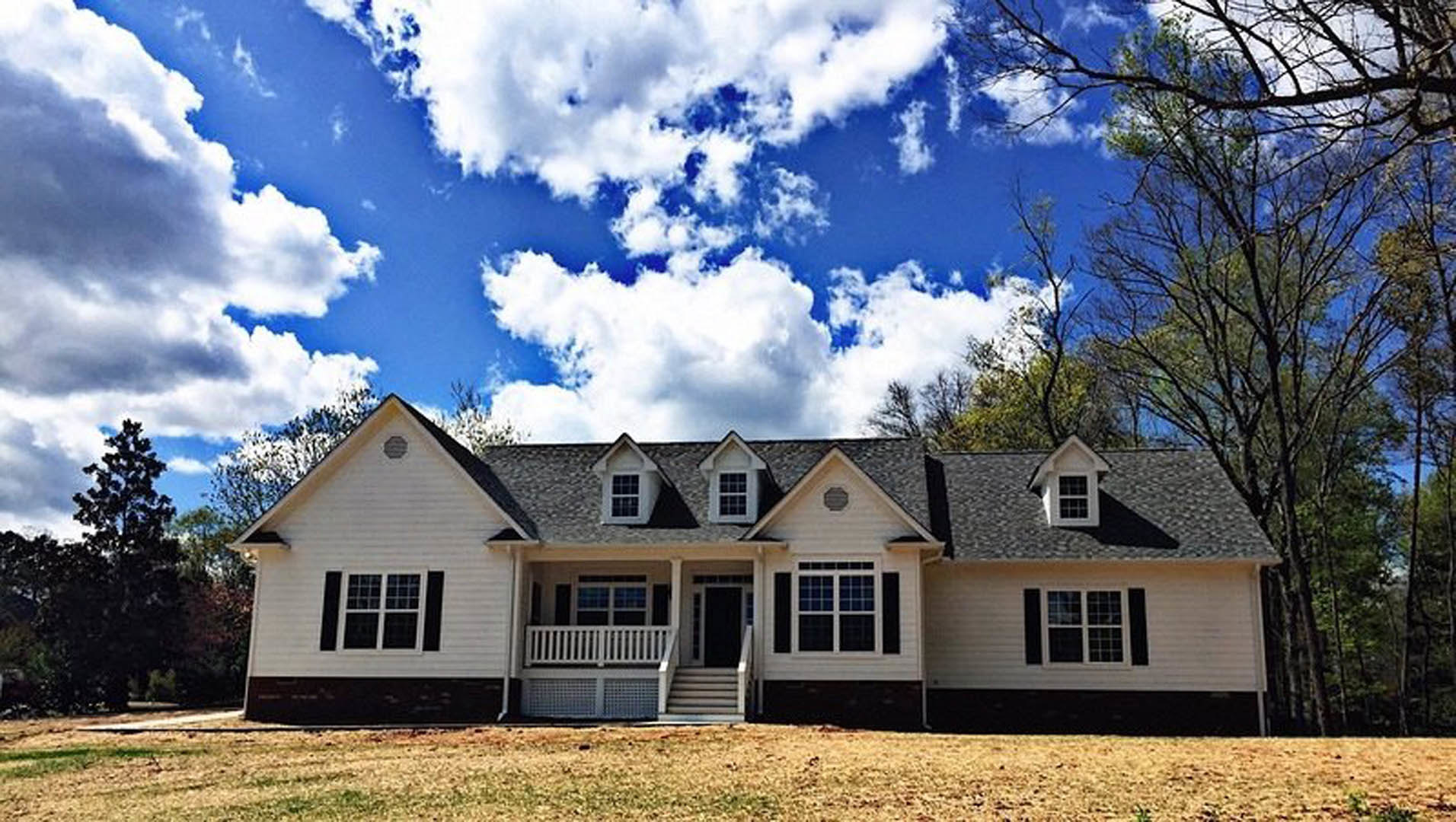 Two-story house with white porch railing, stairs leading to entry, multi-pane windows, black mailbox, green lawn, and mature trees in front yard