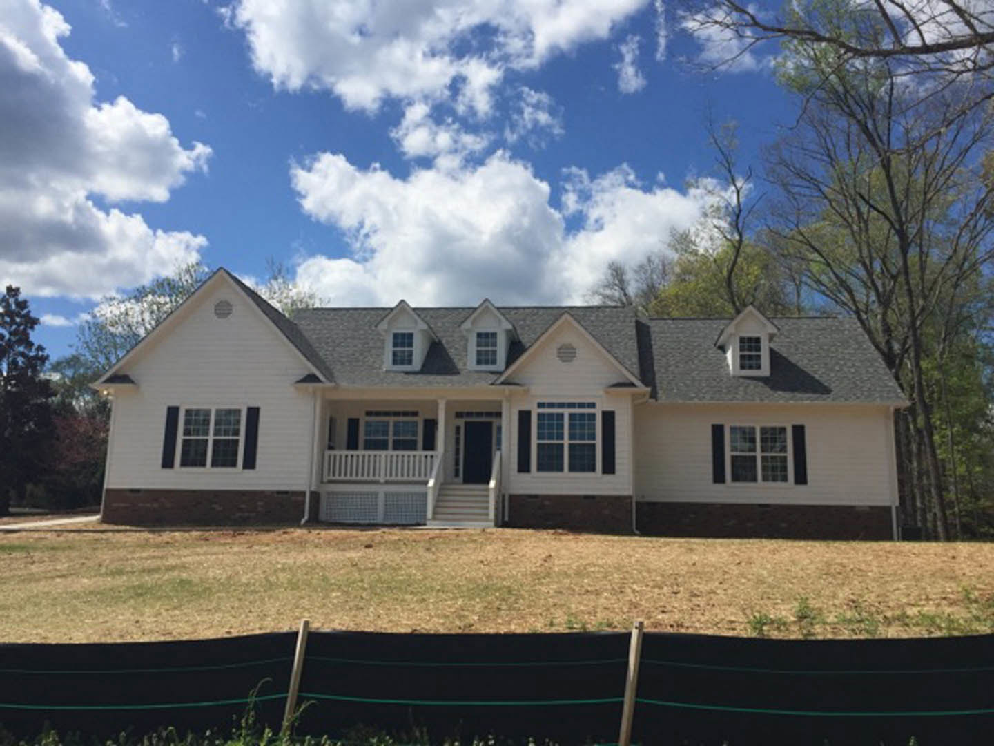 Two-story home with white balcony railing, covered porch, multi-pane windows, wooden fence, and mature trees in front yard