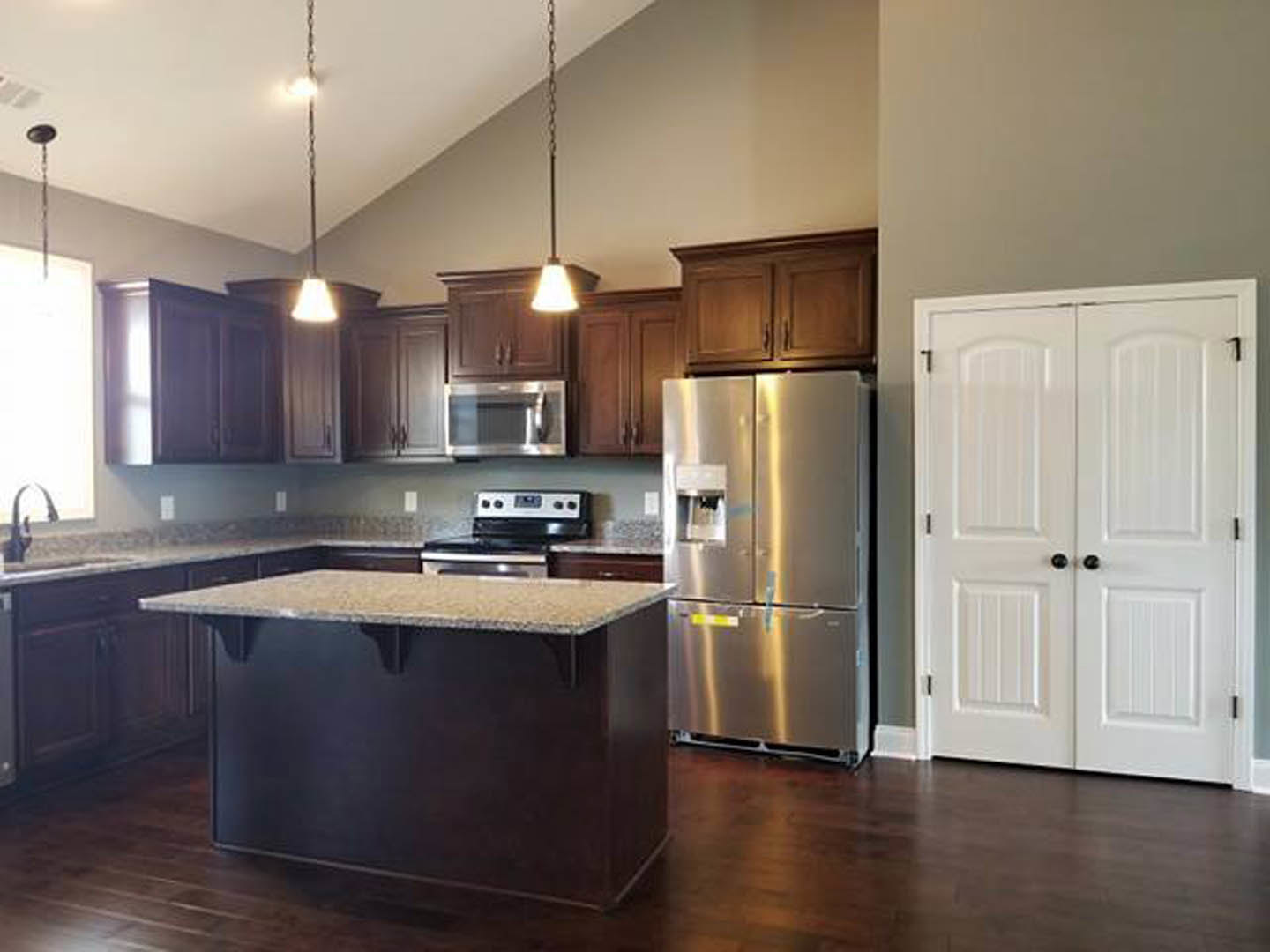 Spacious kitchen featuring a large central island with stone countertop, stainless steel refrigerator, white cabinetry with black knobs, and hardwood flooring