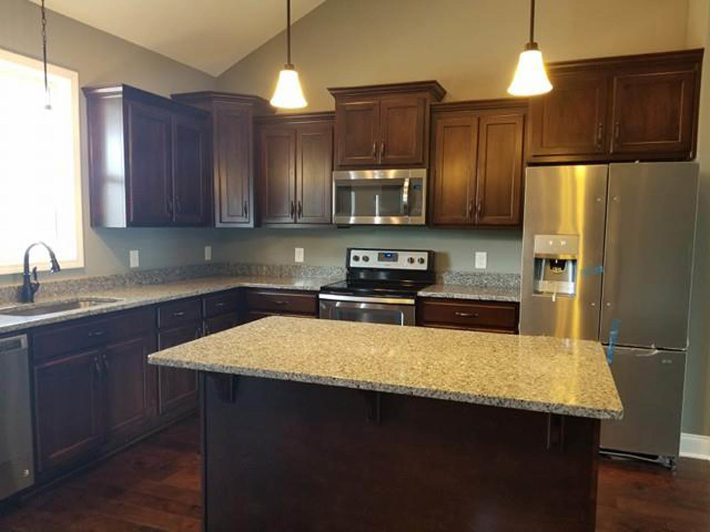 Kitchen with dark wood cabinetry, granite countertops, stainless steel refrigerator with water dispenser, metal shelving, stove, and sink