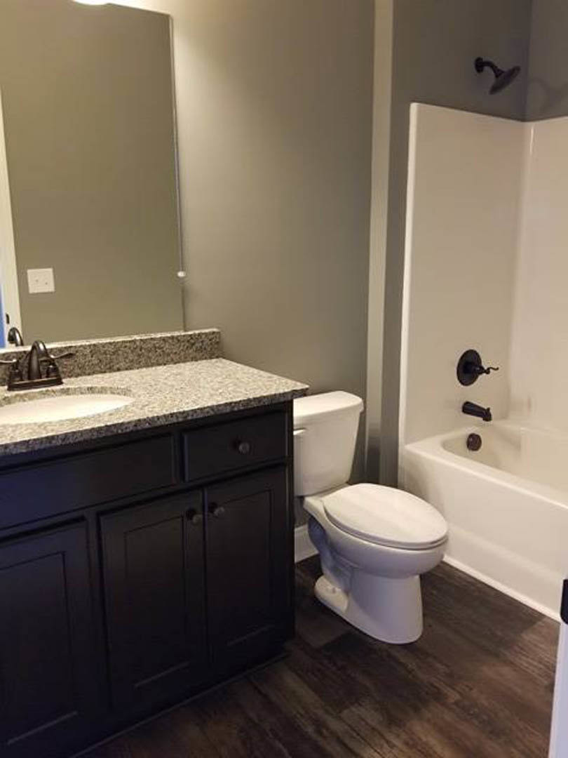 Modern bathroom featuring a white toilet with closed lid, black vanity cabinet with drawers, rectangular sink, wall-mounted faucet, and light-colored tile flooring.